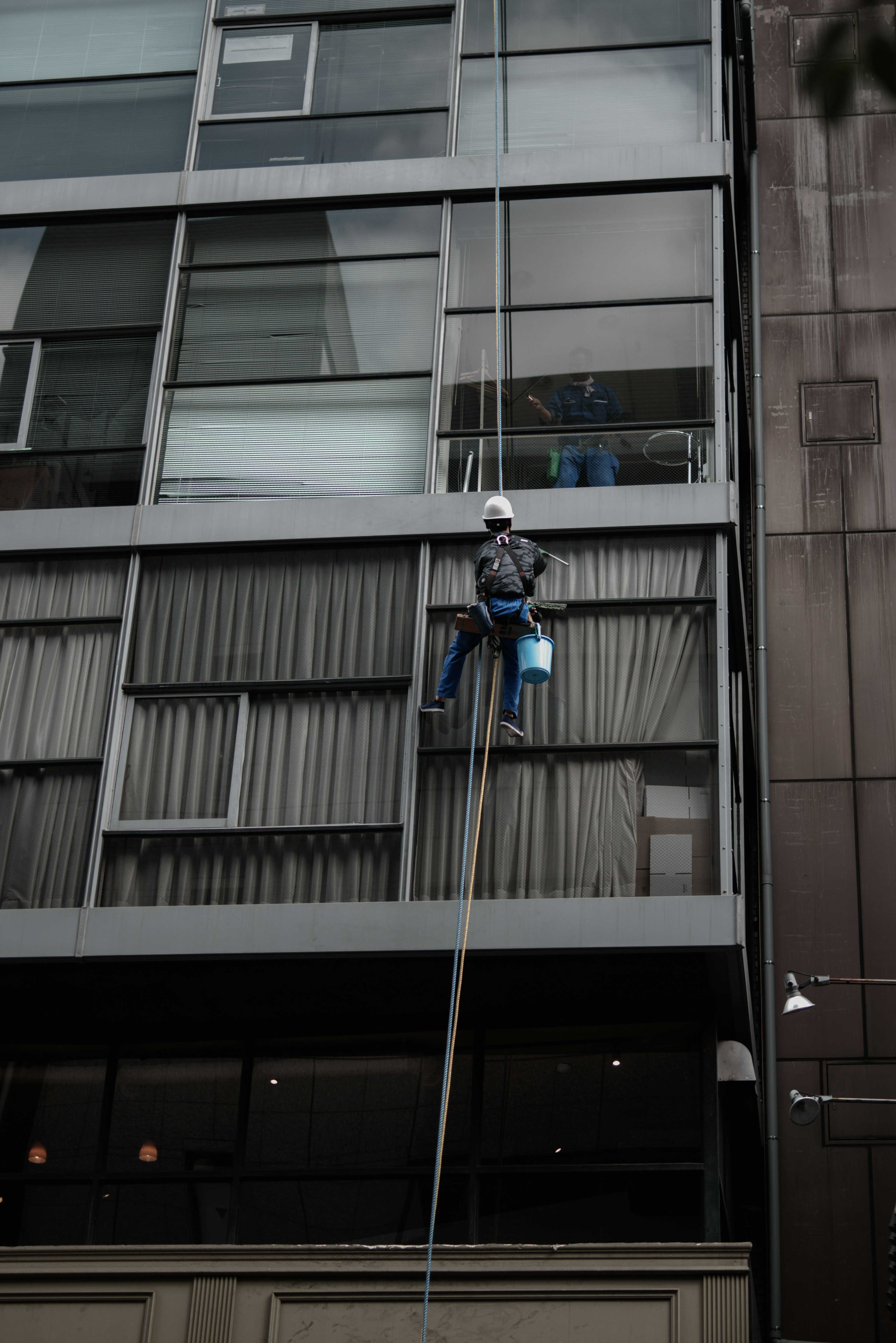 Arbeiter, der Fenster reinigt und an einem Seil von einem modernen Gebäude absteigt