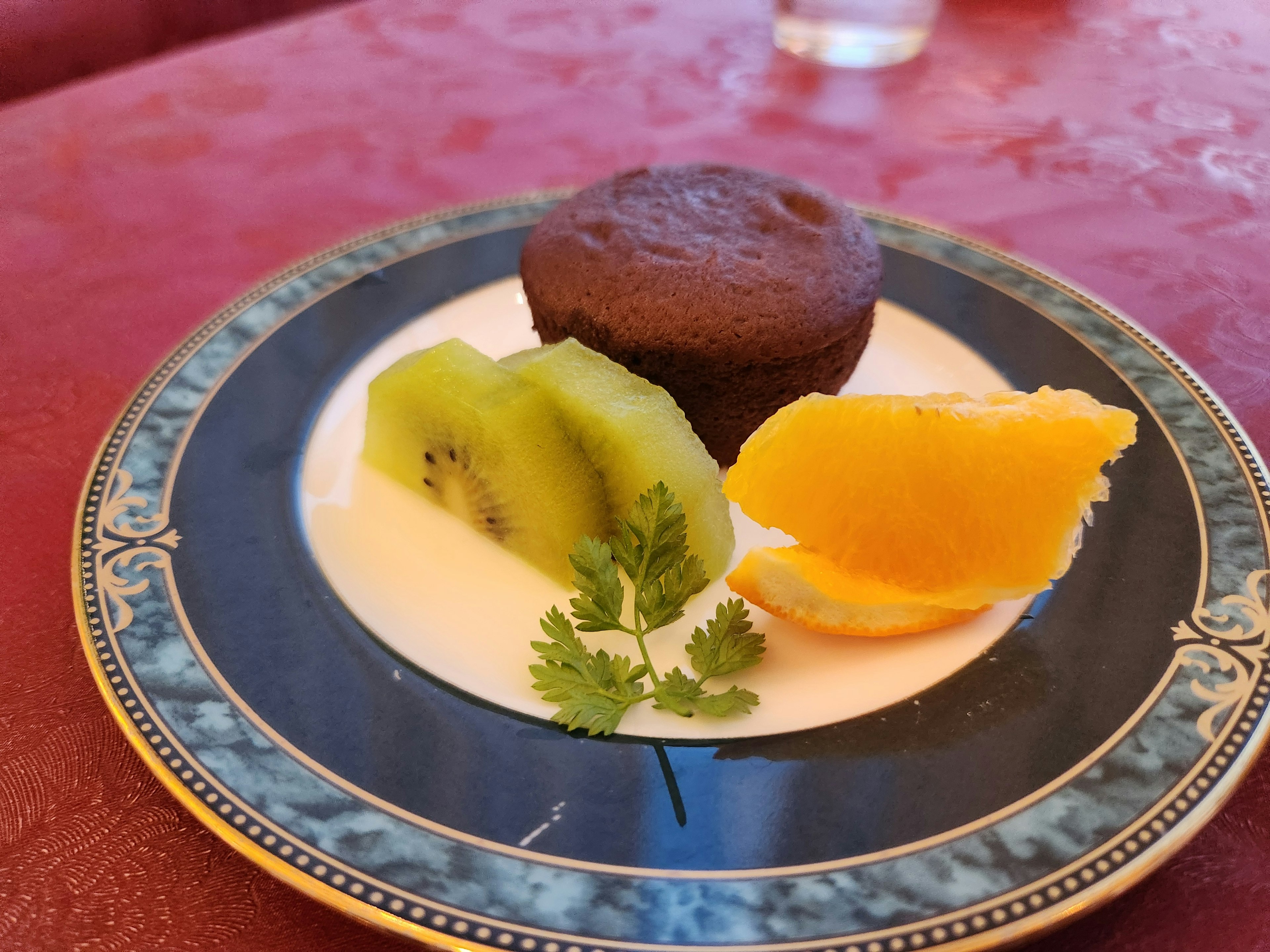 Une assiette avec un muffin au chocolat accompagné de tranches de kiwi et d'orange, garni de coriandre fraîche