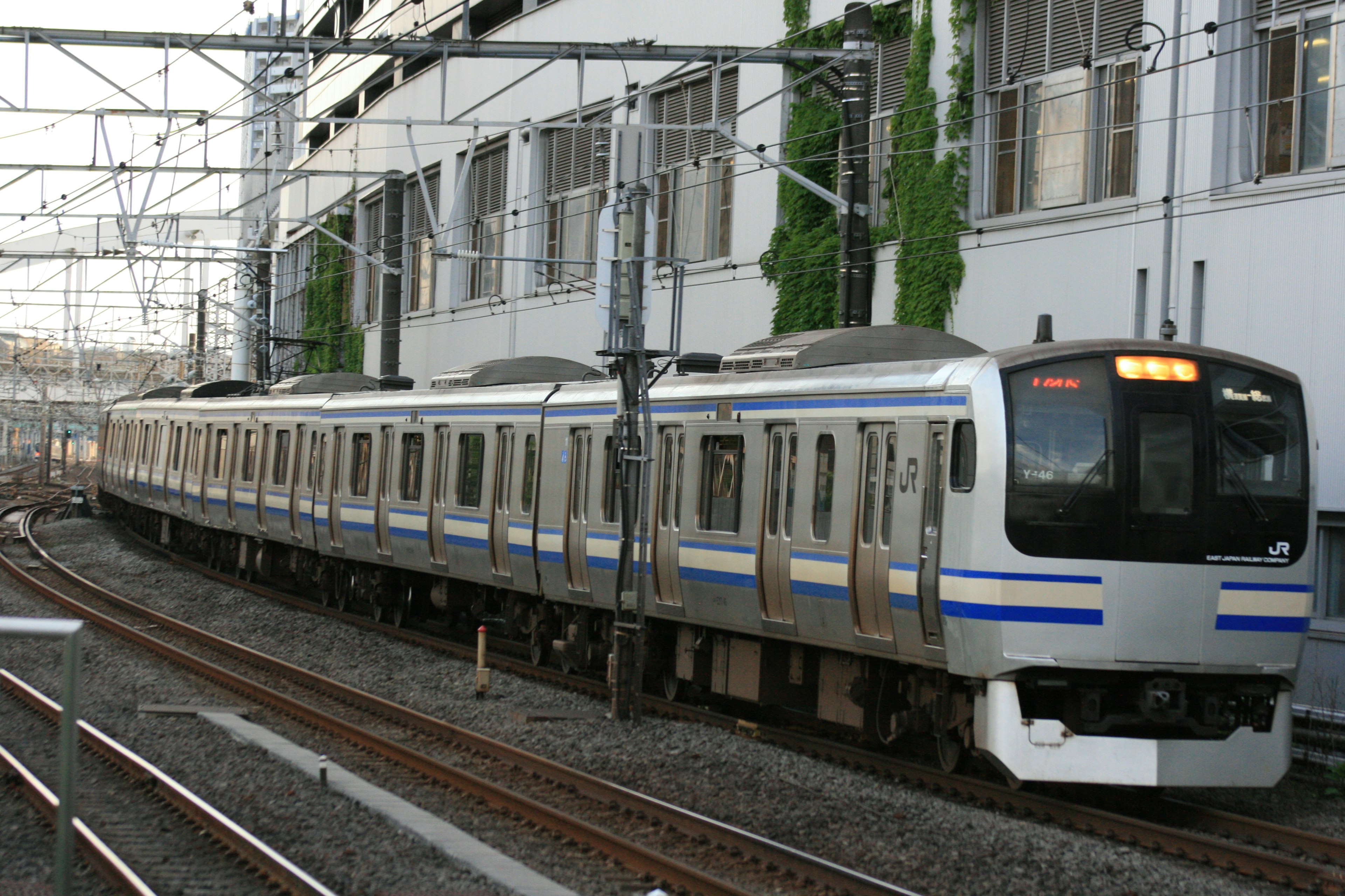 Train argenté tournant un virage avec des voies ferrées et des bâtiments en arrière-plan