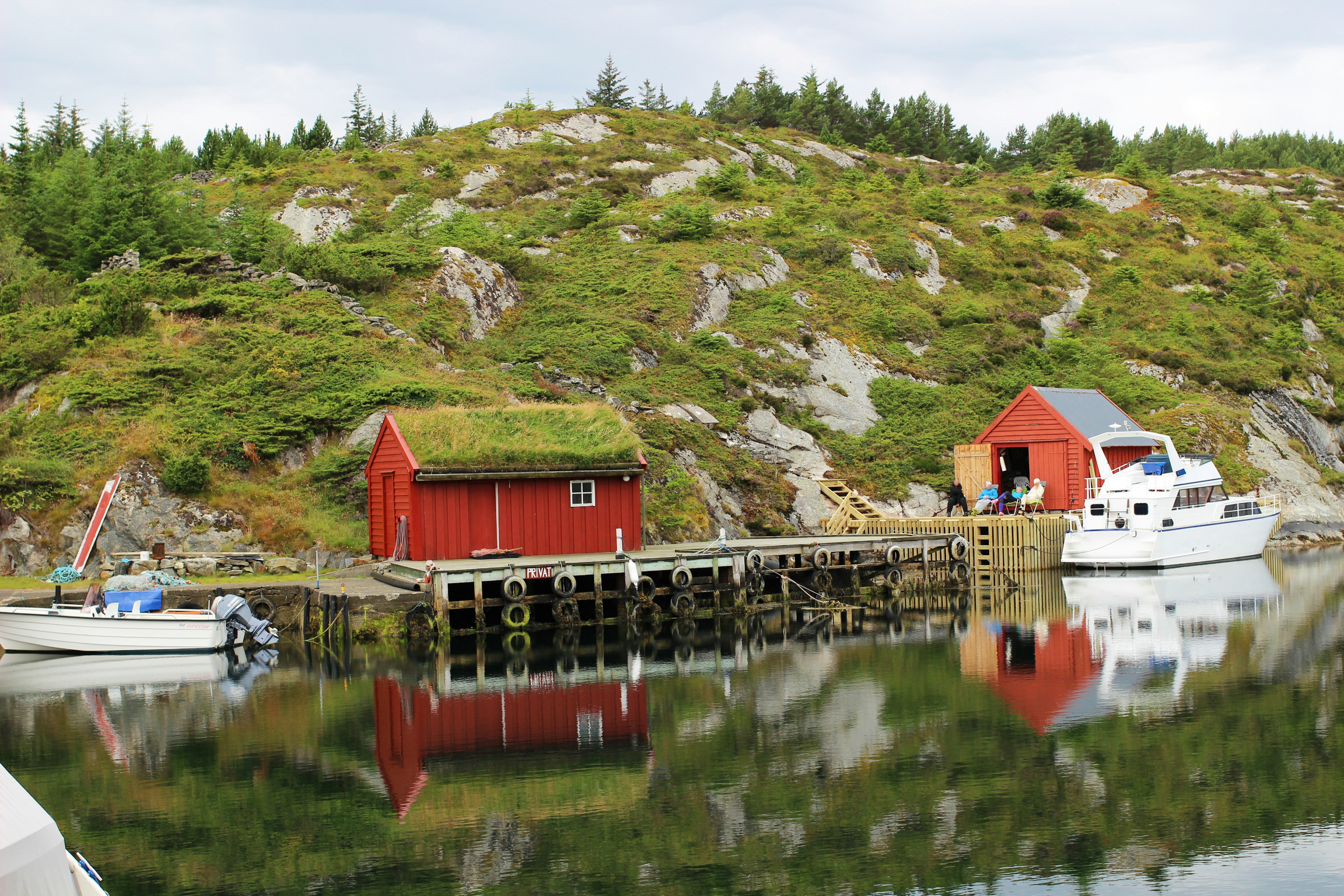 A serene harbor scene with a red cabin and boats near green hills