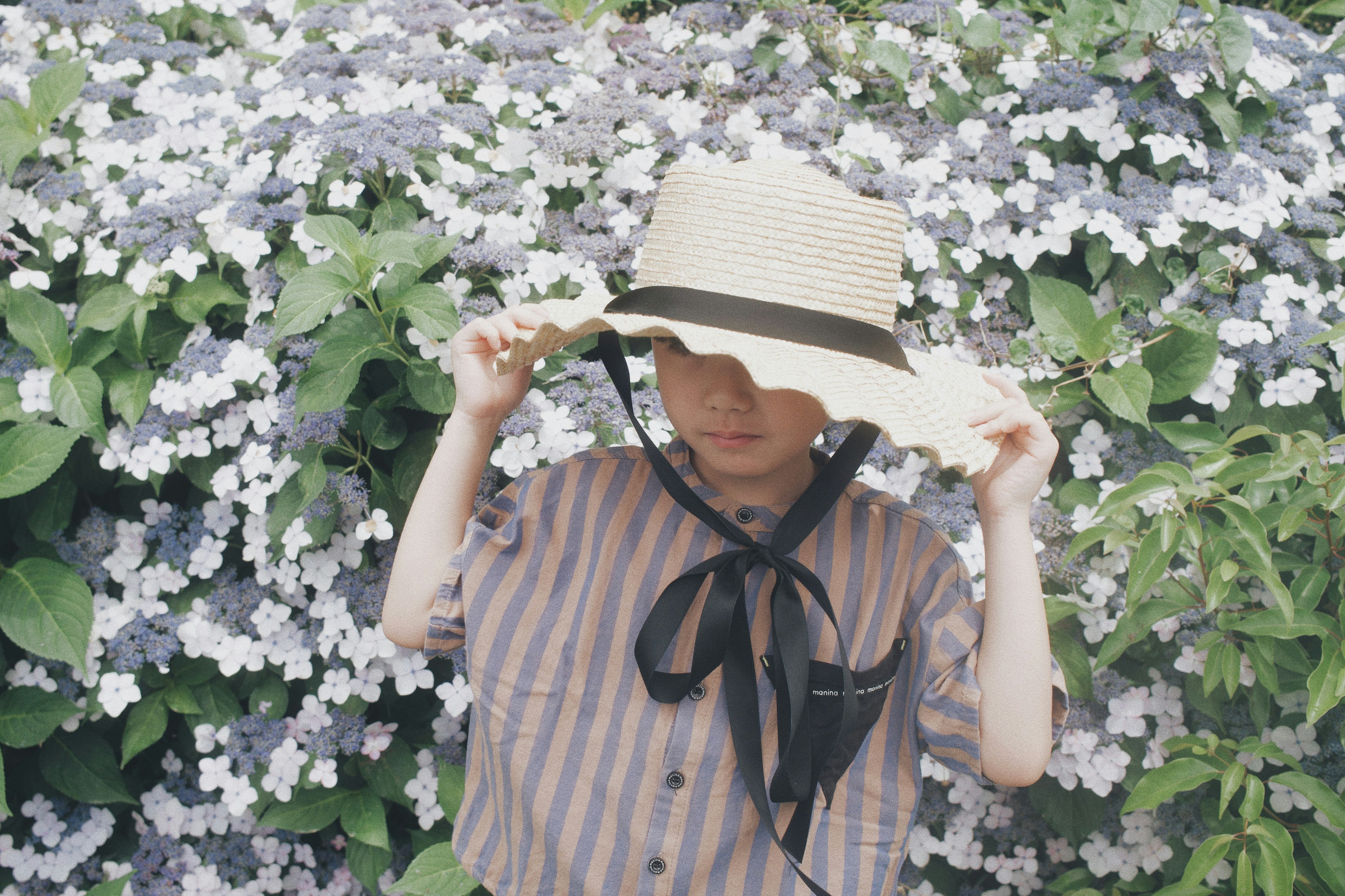 帽子をかぶった子供が花の前でポーズをとっている