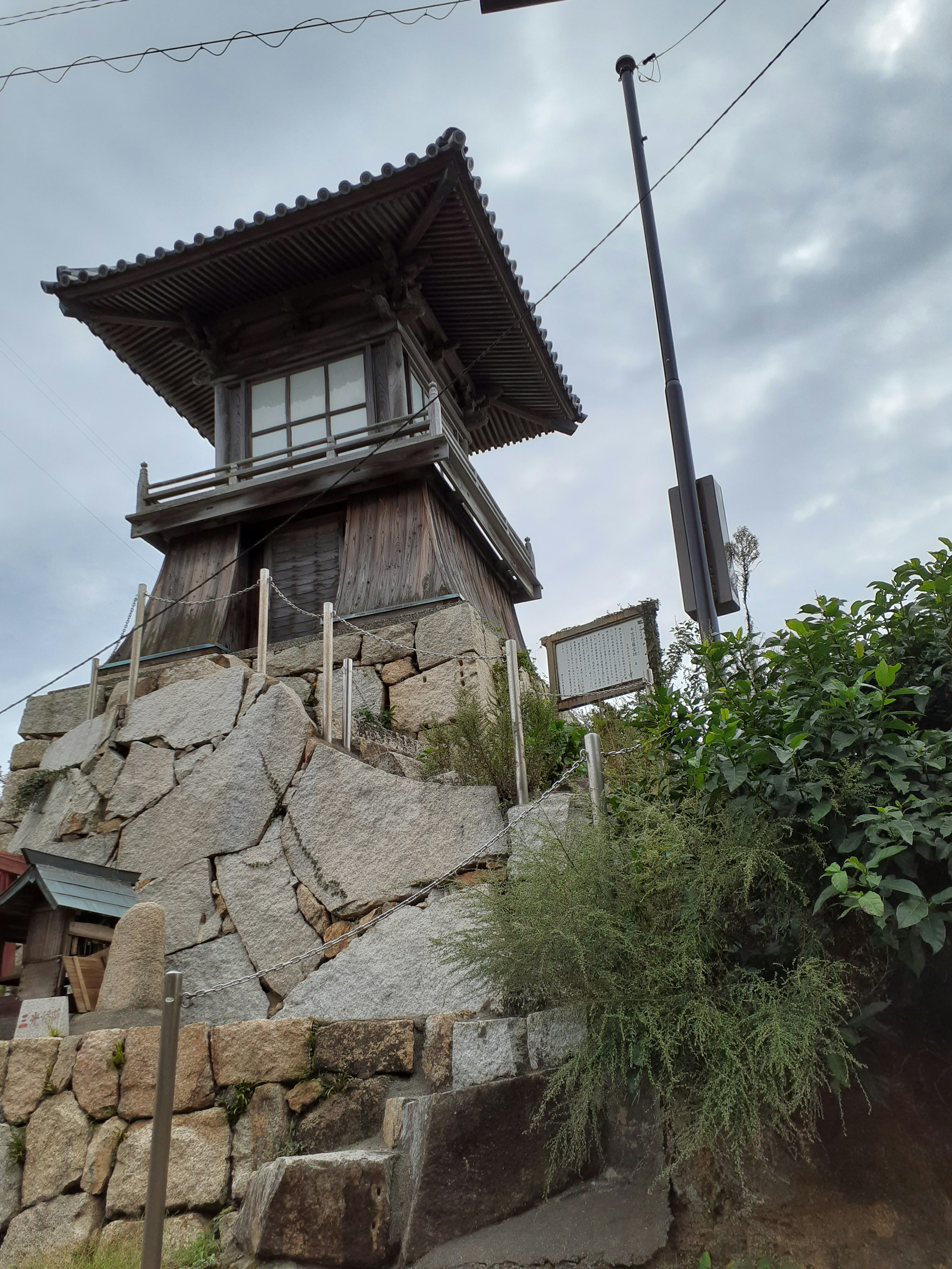 Traditioneller japanischer Turm auf einem Steinfundament mit bewölktem Himmel