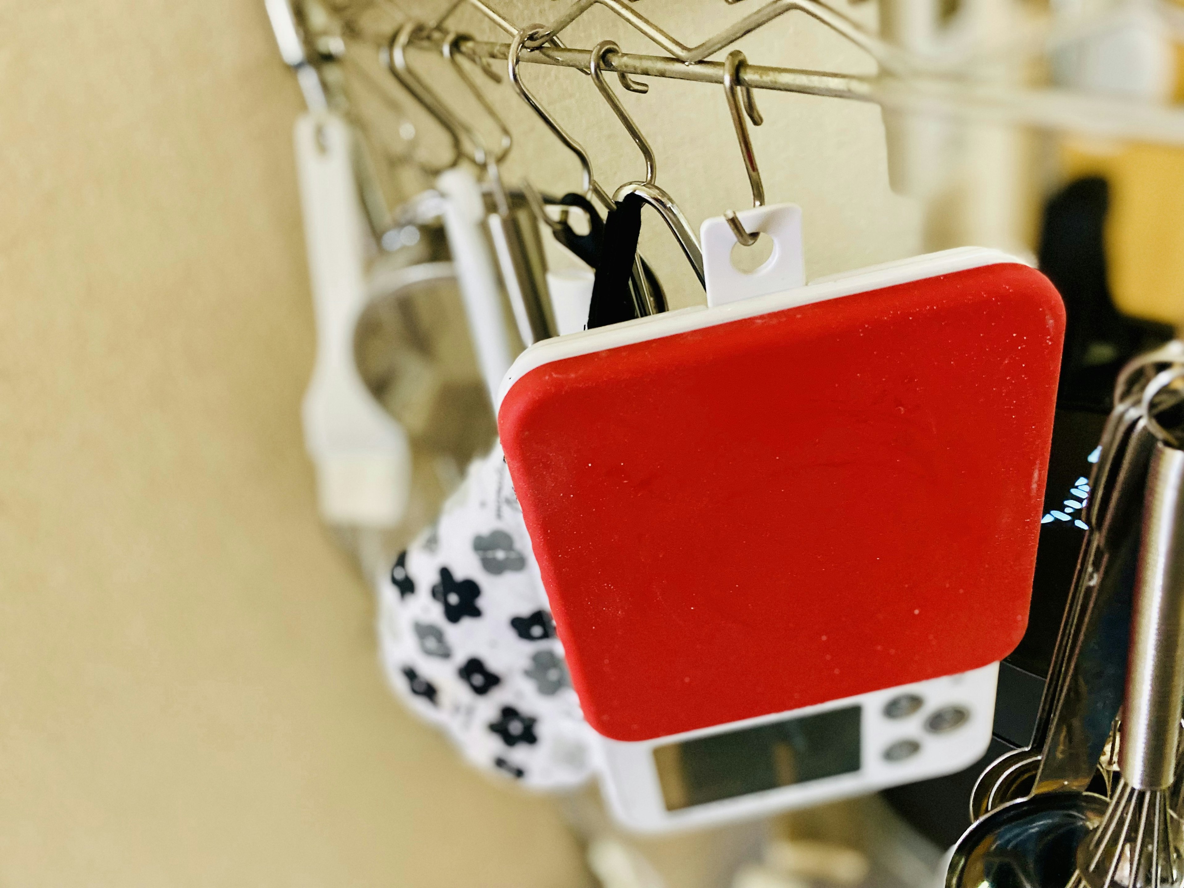 Red square kitchen scale hanging alongside a black and white floral apron in a kitchen setting