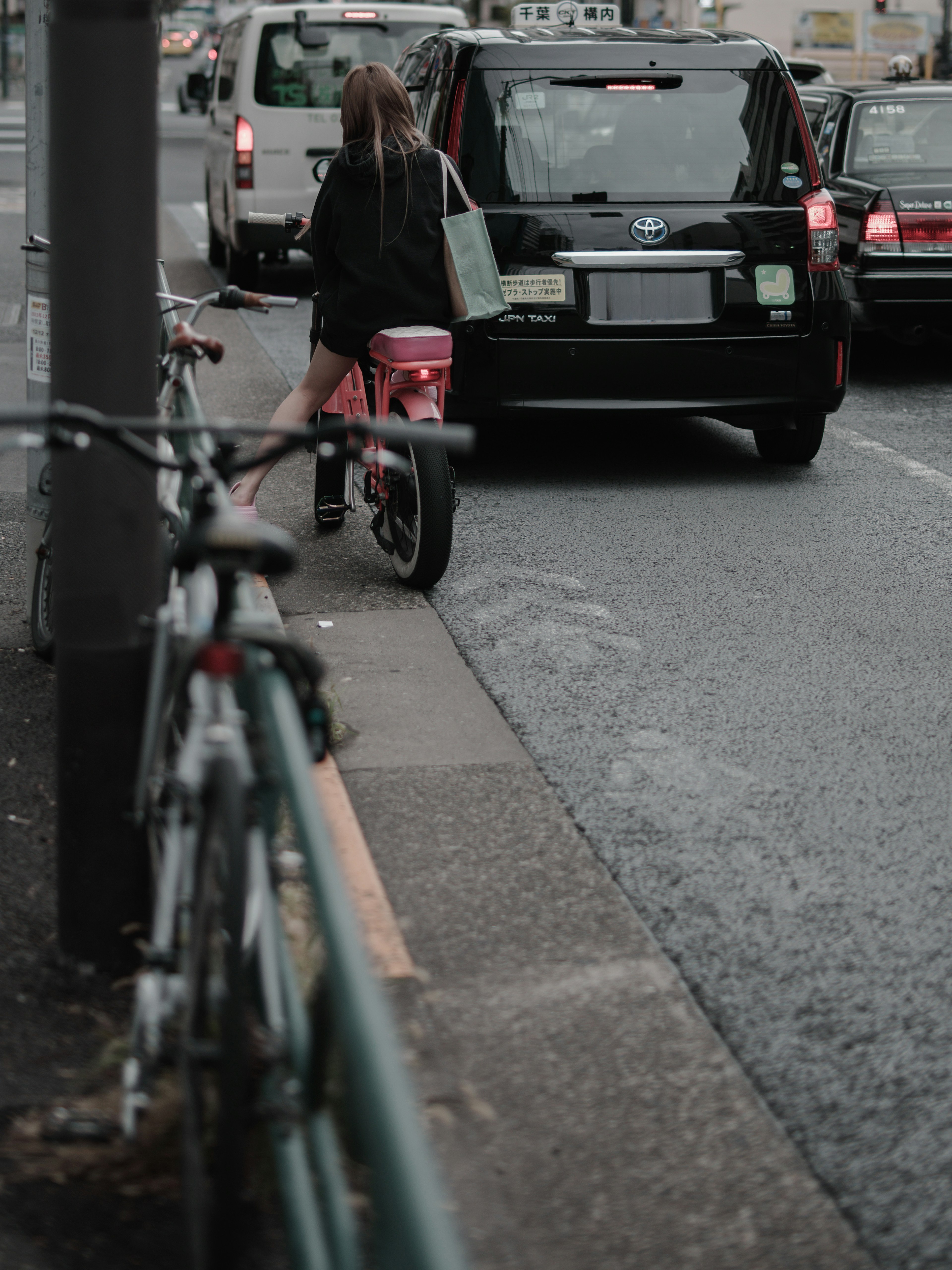 A woman standing near a black car with bicycles lined up on the street