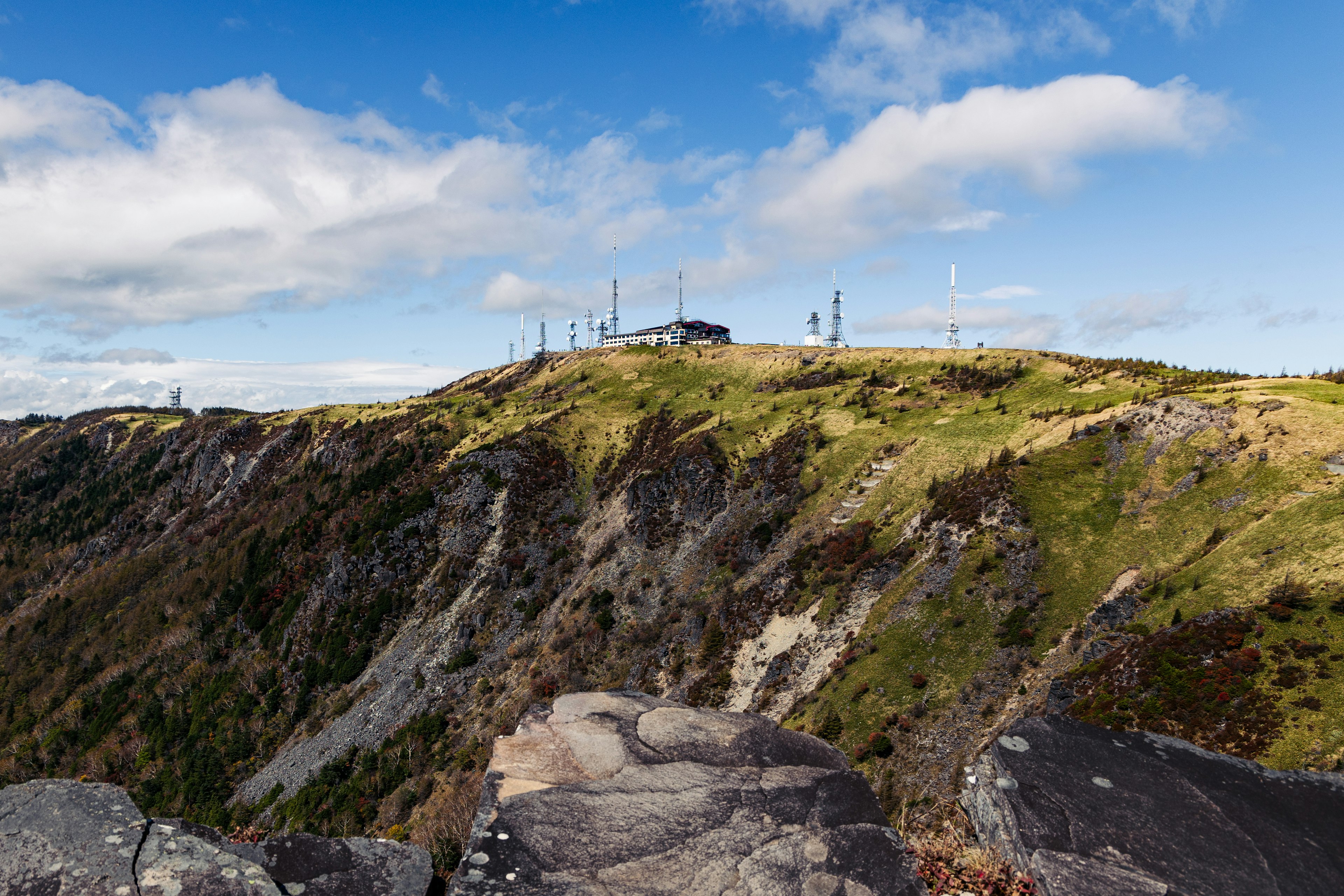 Landscape photo featuring a blue sky and green hills with buildings and wind turbines in the distance