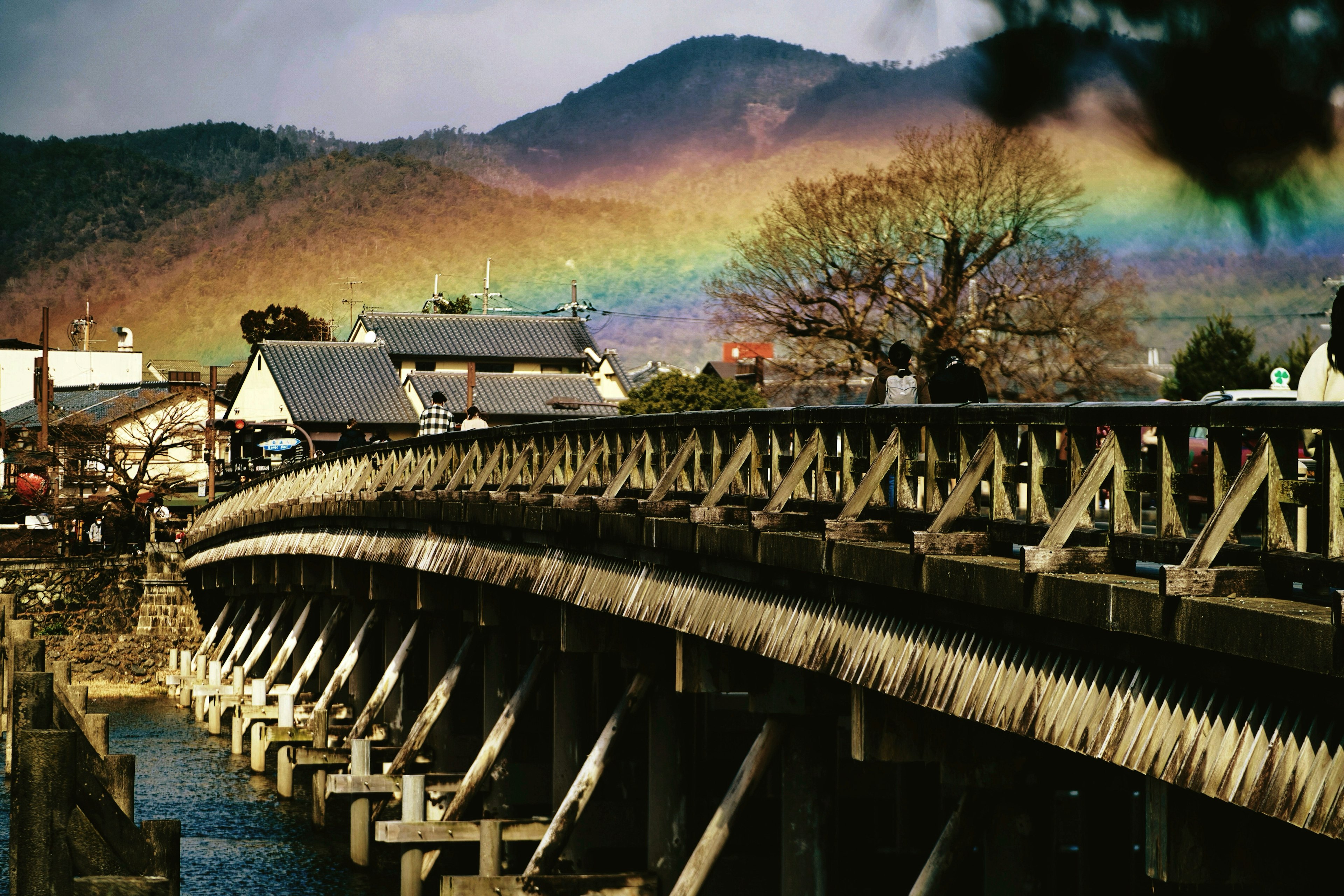 Puente de madera con edificios y un arcoíris sobre las montañas