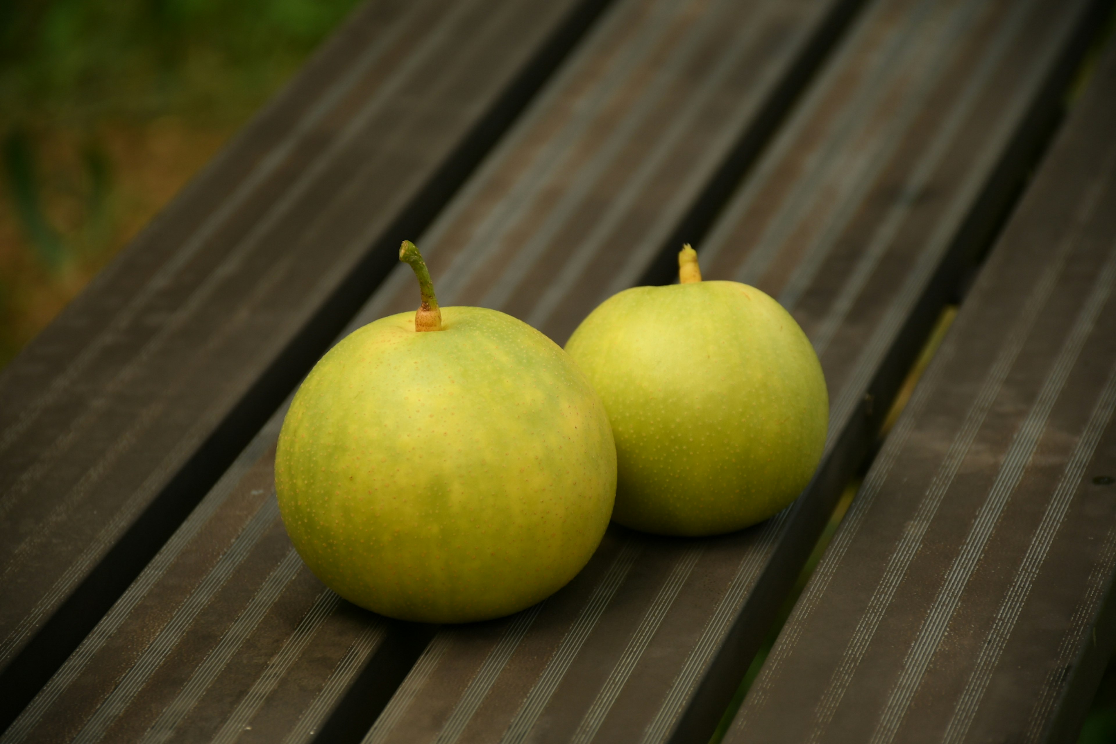 Two green apples resting on a wooden table