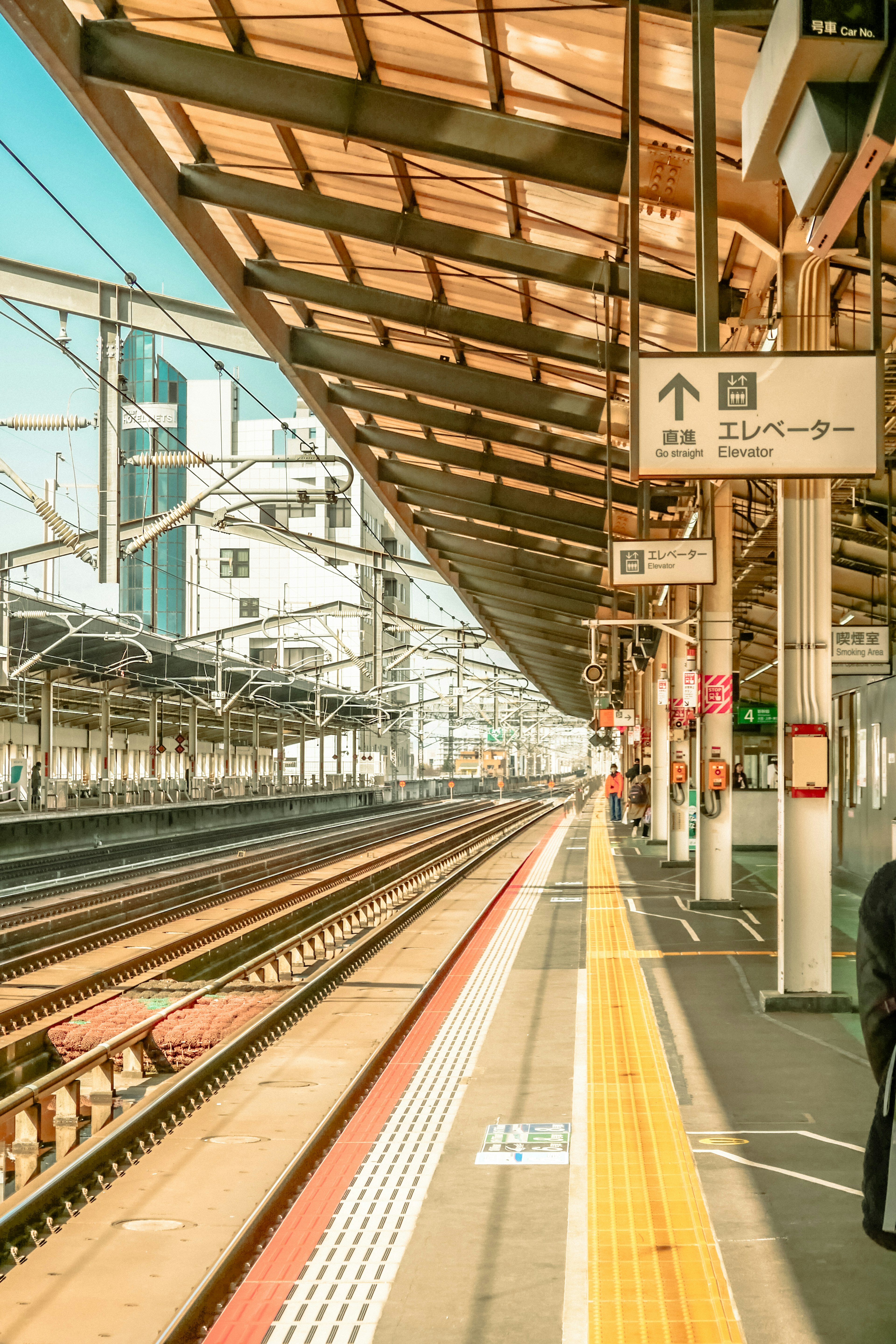 View of a train station platform with visible tracks and a roofed structure featuring signs