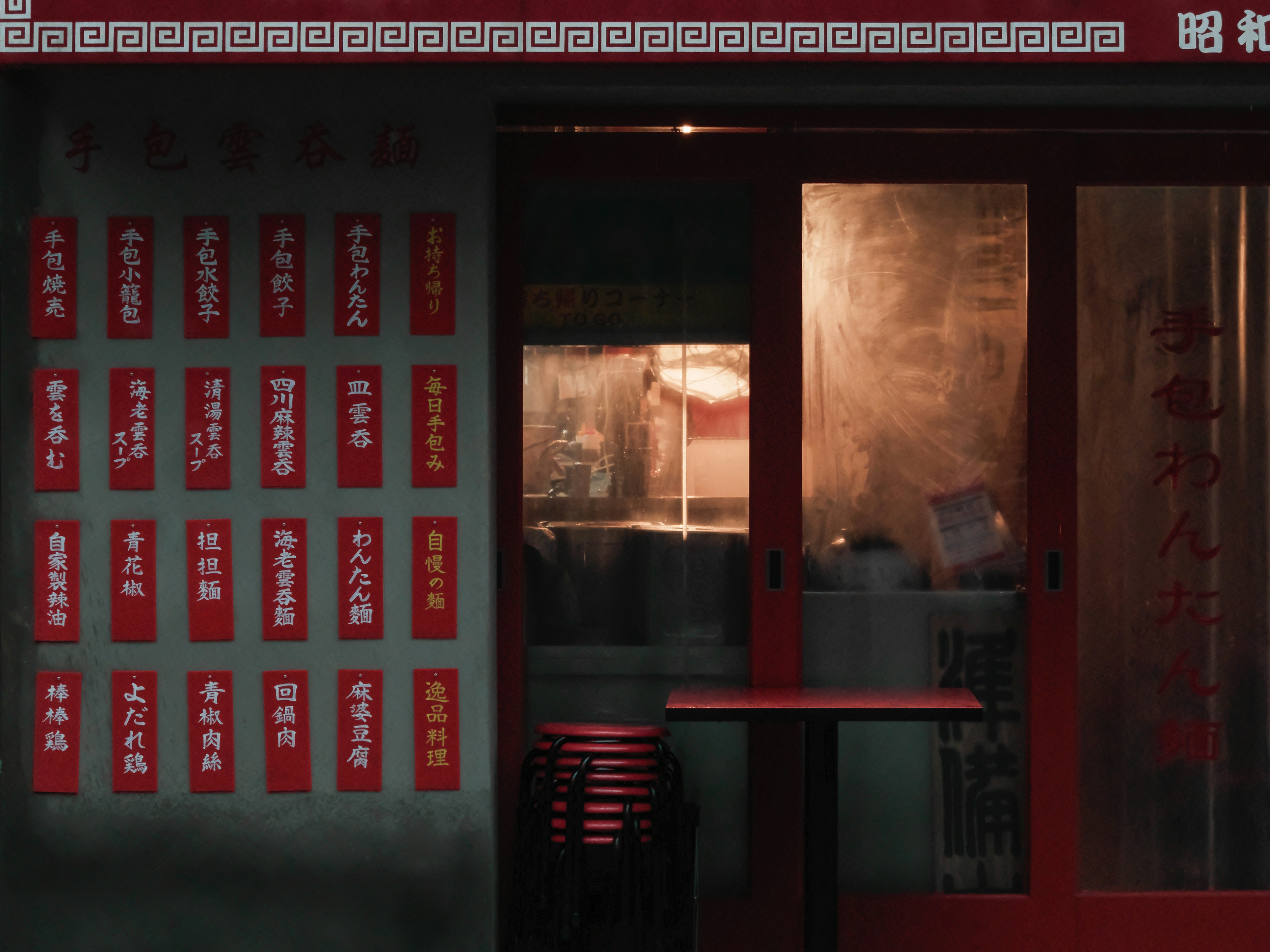 Entrance of a small eatery with red signs showcasing menu items and a glimpse inside