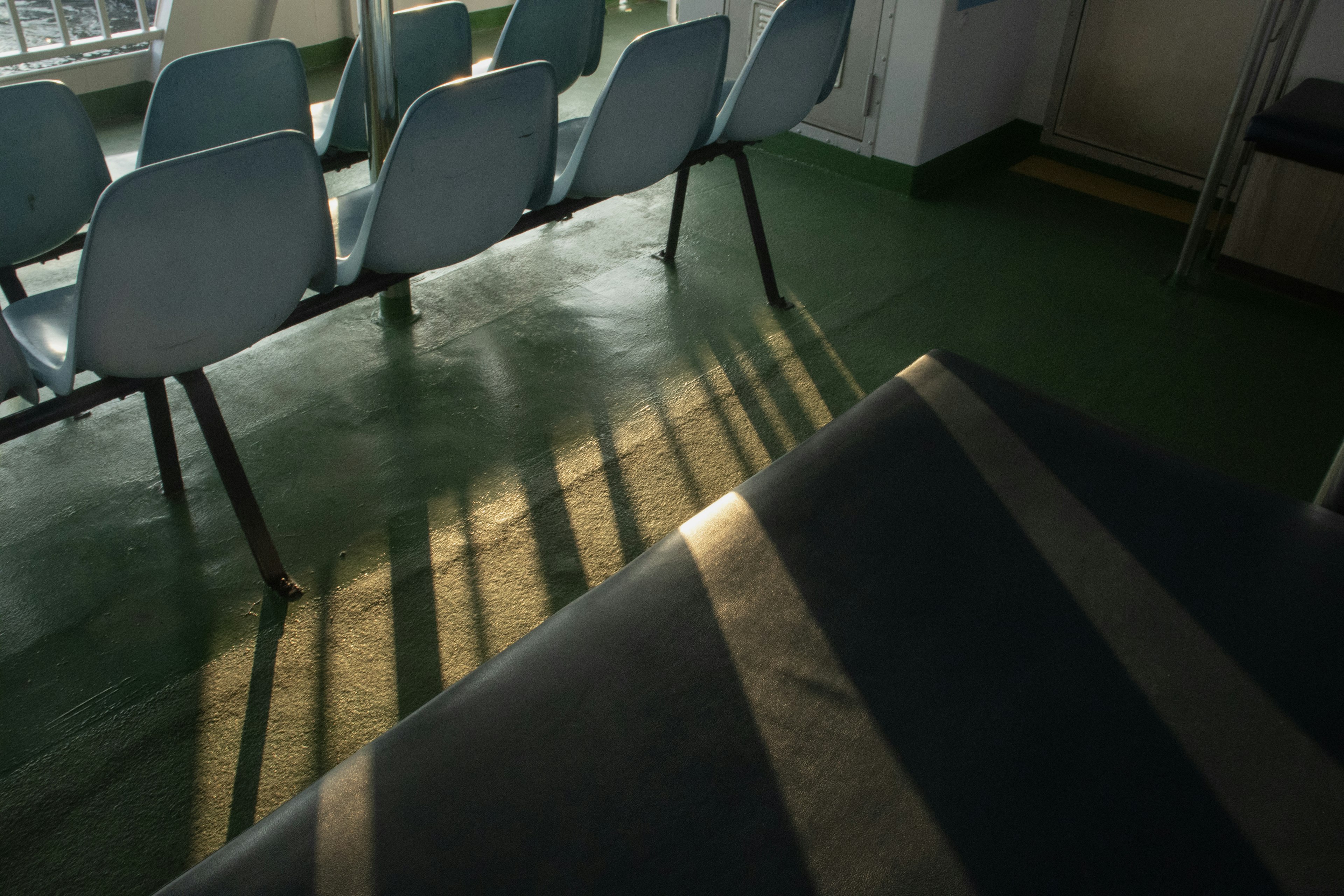 Parte de una sala de espera con sillas azules luz solar proyectando sombras en el suelo verde