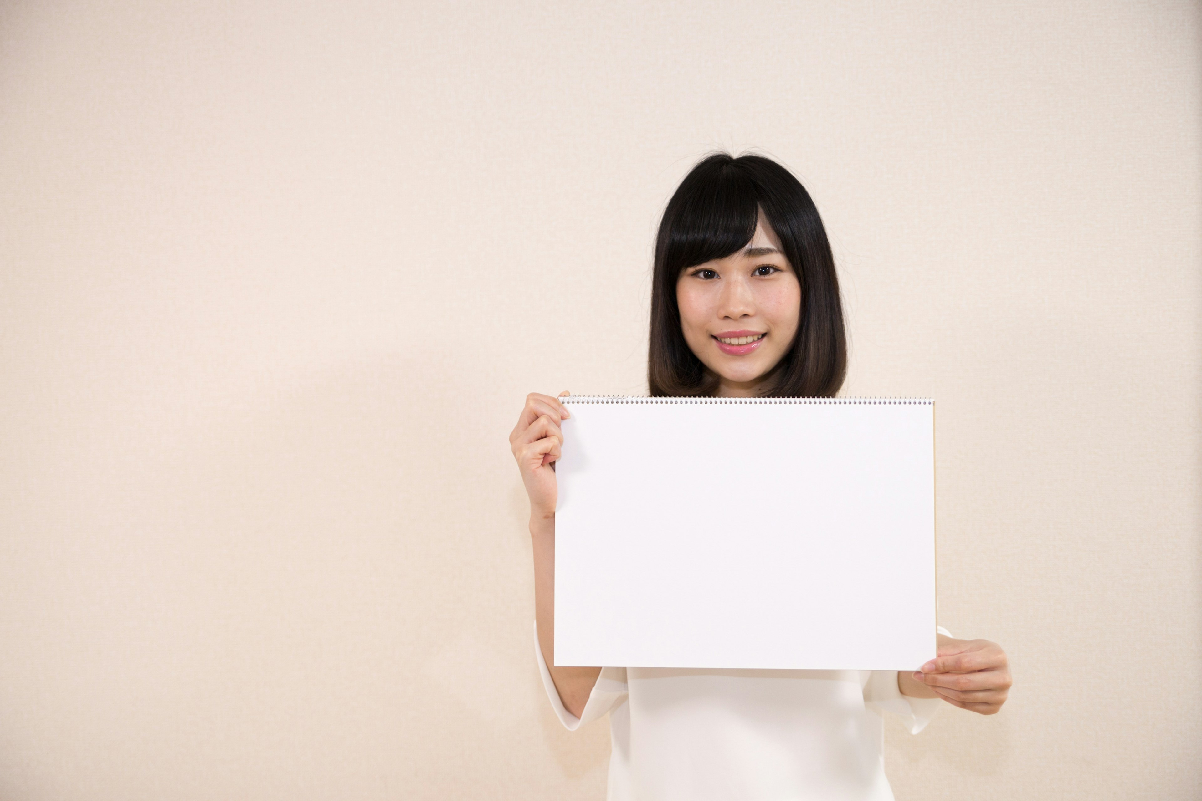 Woman holding a blank white board in front of a light background