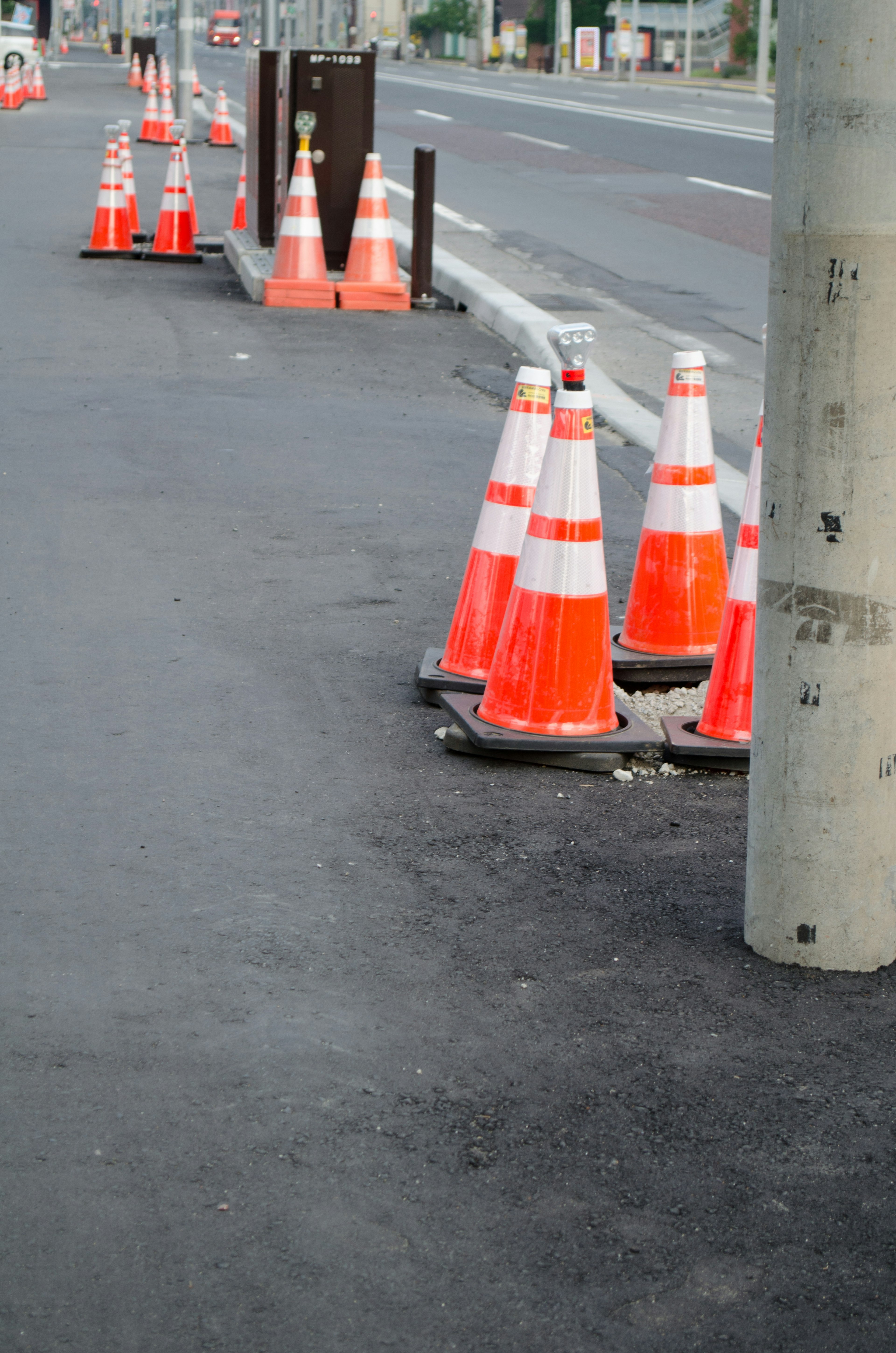 Photo of orange and white traffic cones lined up along the roadside next to a utility pole