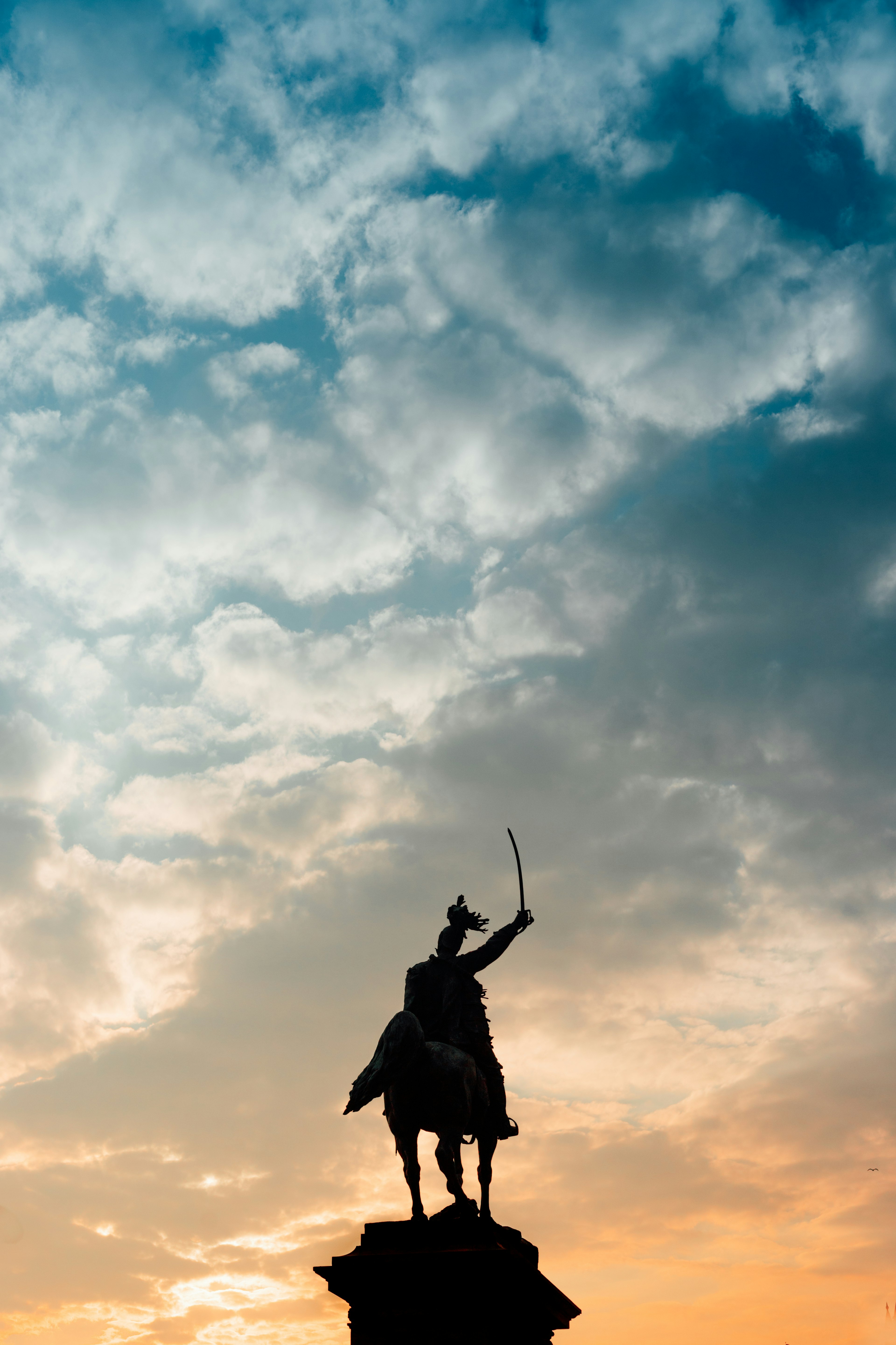 Silhouette of a knight statue holding a sword against a colorful sky