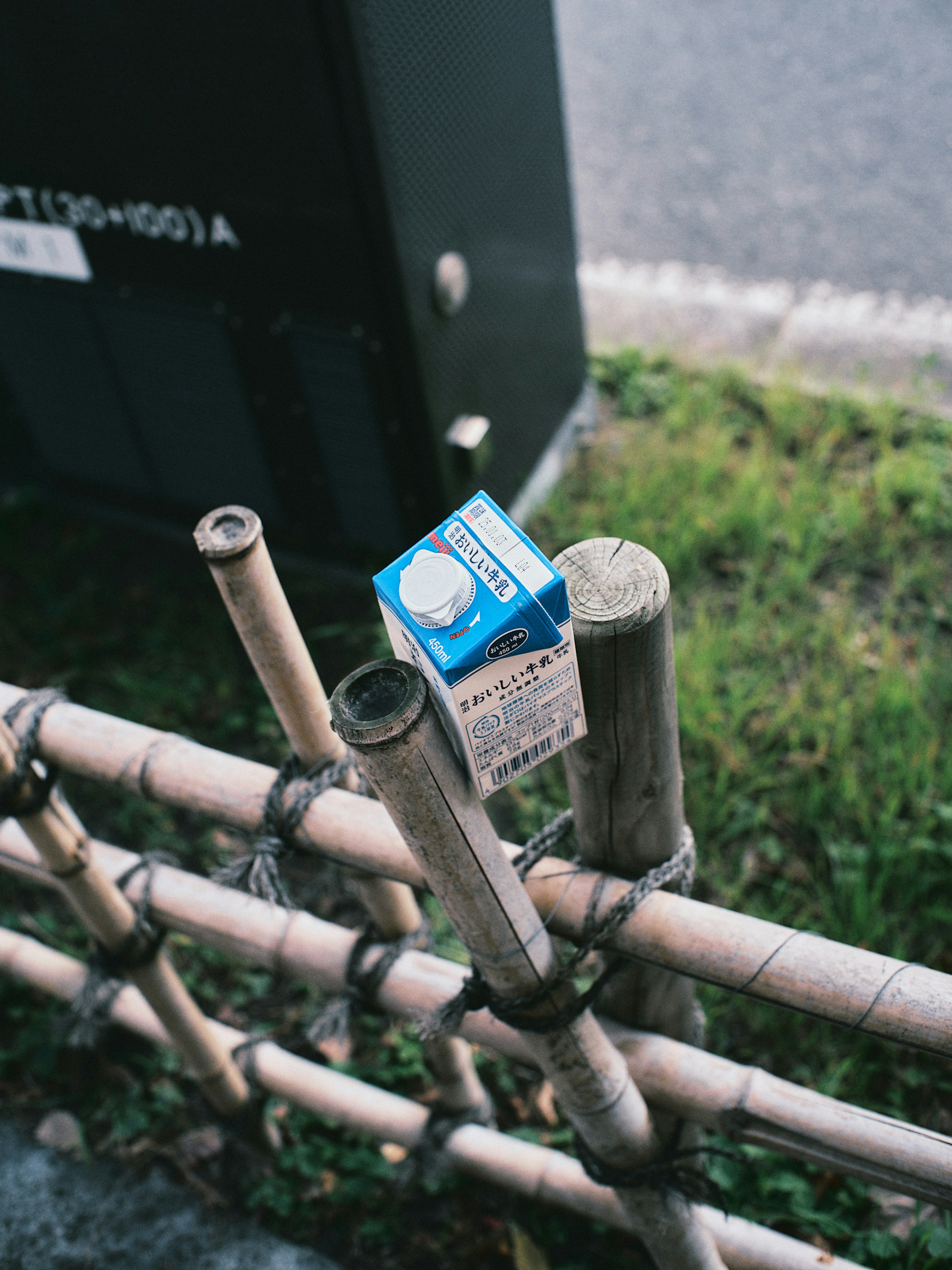 Carton de lait bleu posé sur une clôture en bambou avec de l'herbe environnante