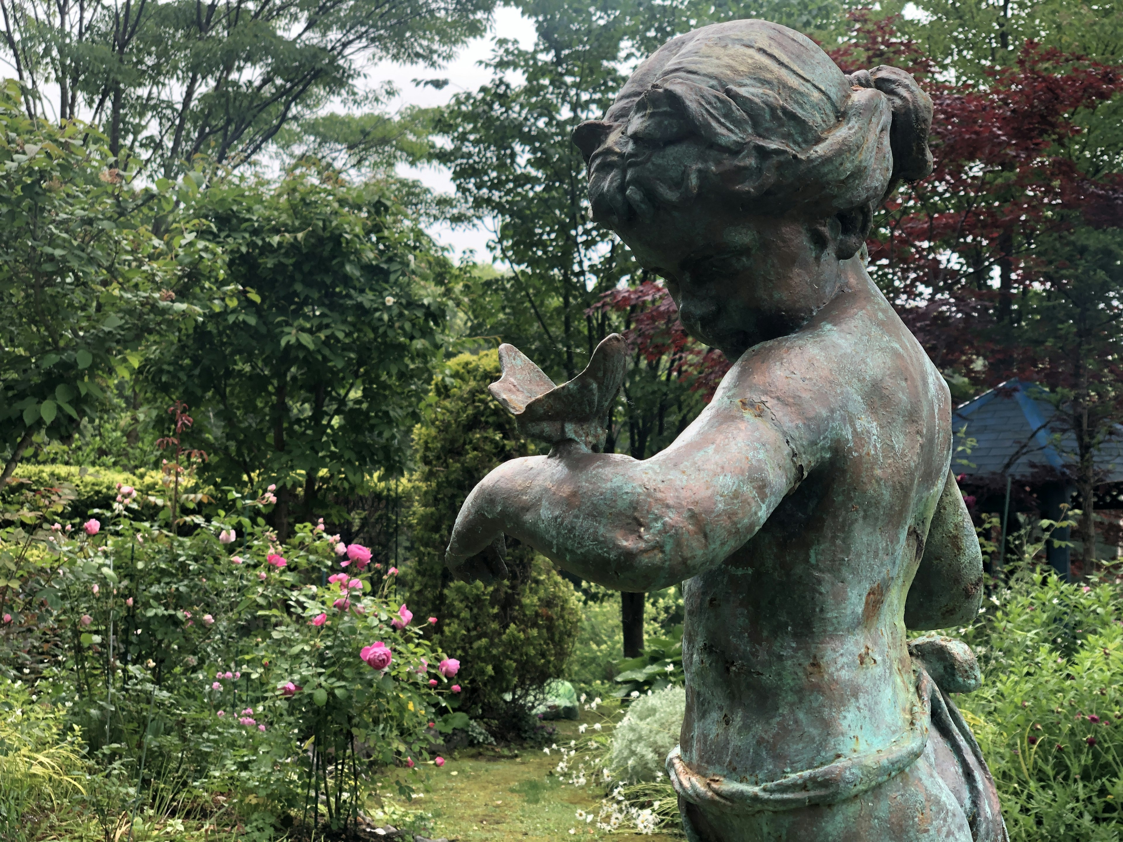 Bronzestatue eines Mädchens in einem Garten umgeben von bunten Blumen