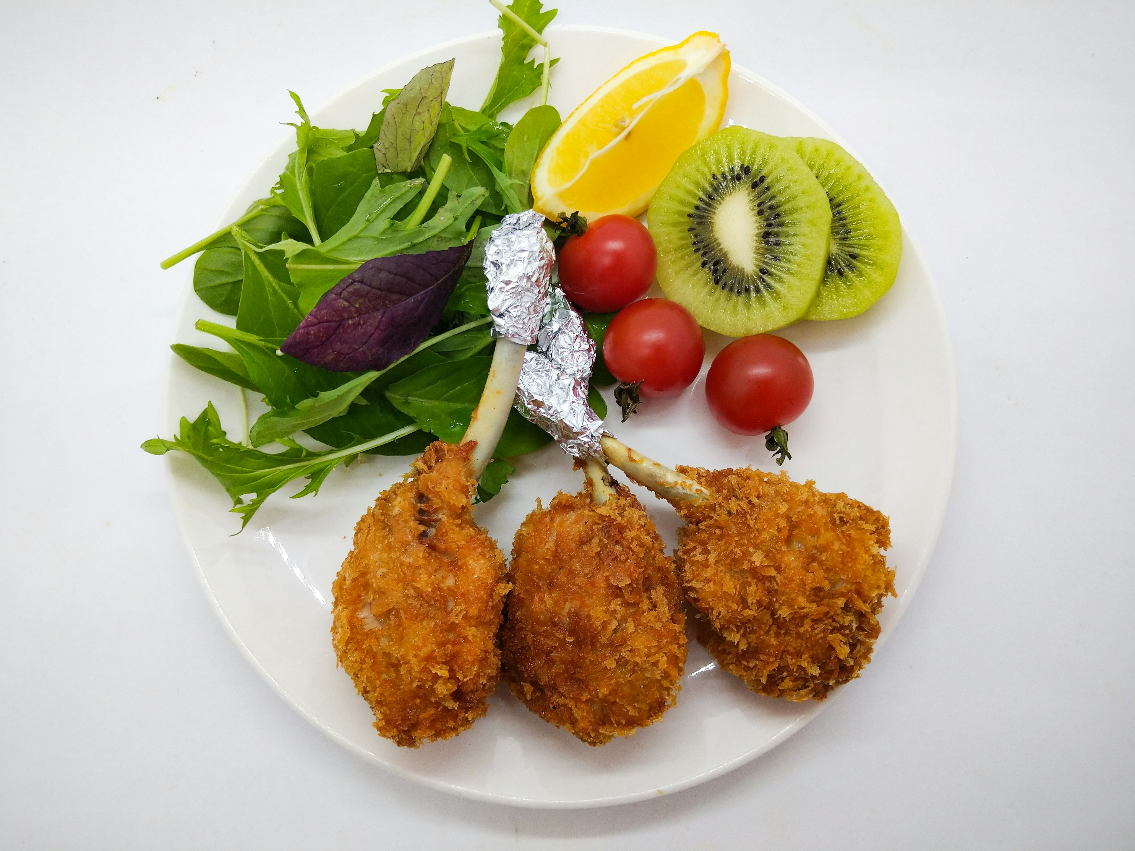 Plated fried chicken drumsticks with salad and fruits