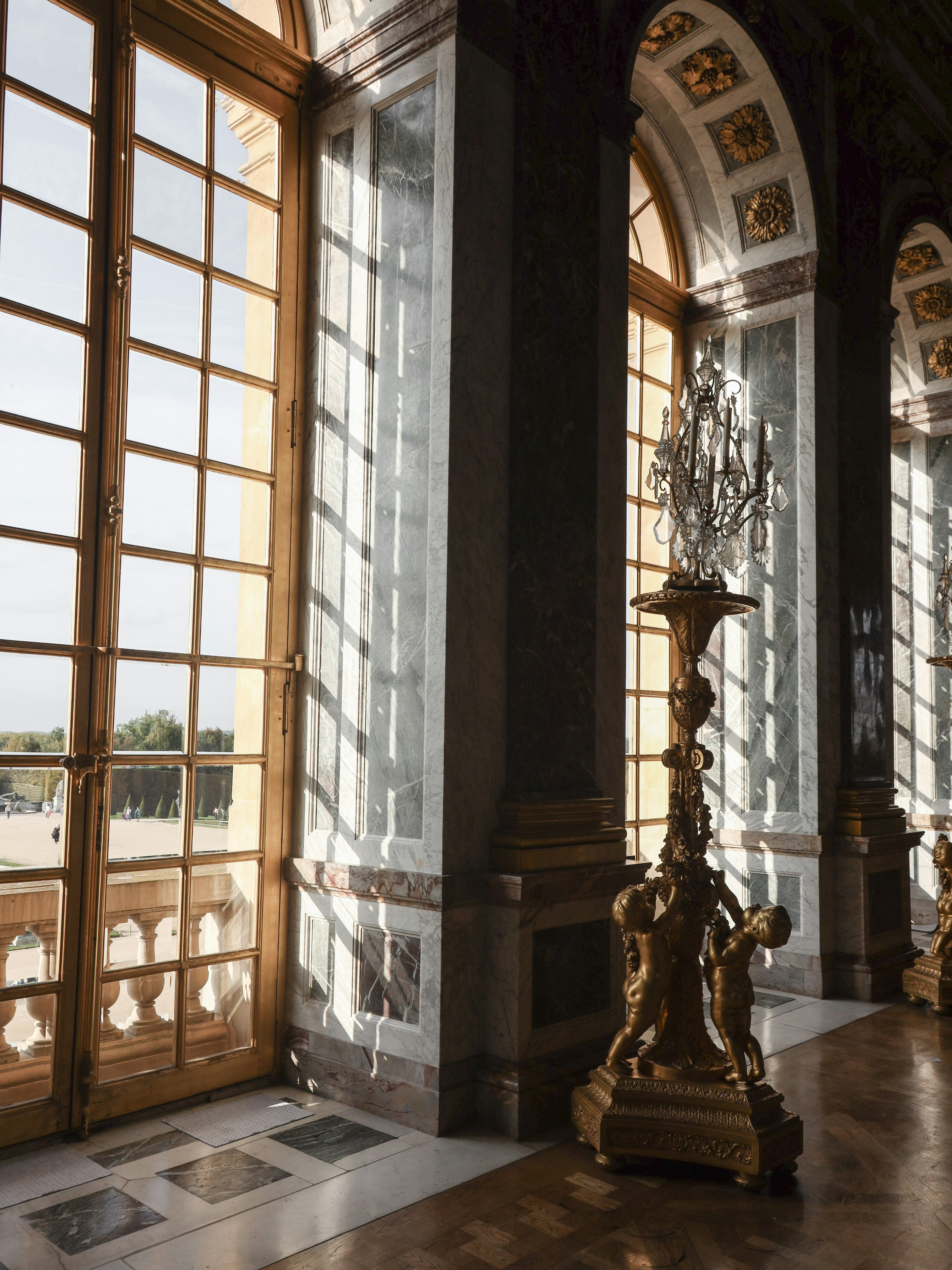 Interior of the Palace of Versailles featuring an ornate chandelier large windows and intricate decor