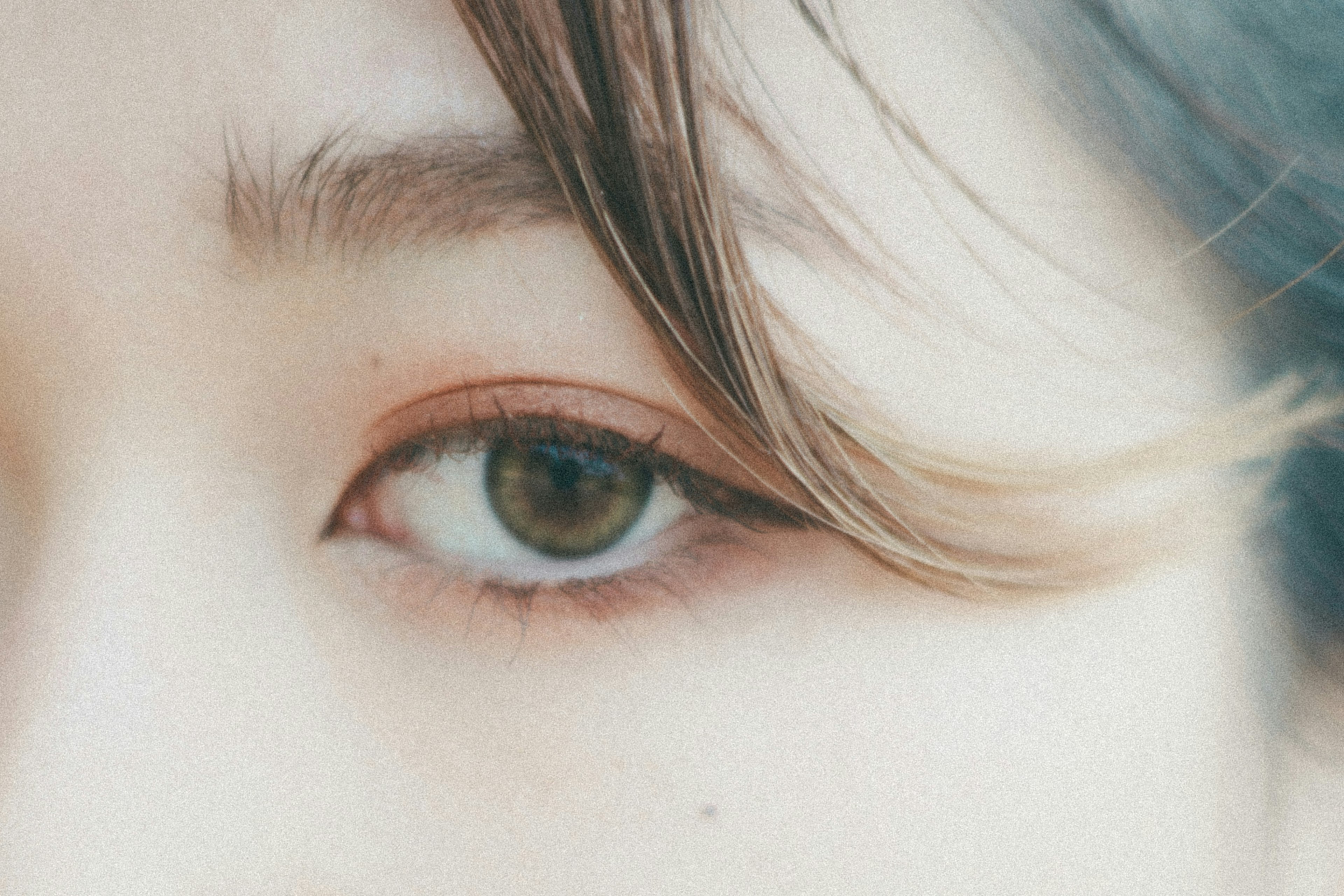 Close-up of a woman's eye featuring a greenish-brown iris and smooth eyelashes