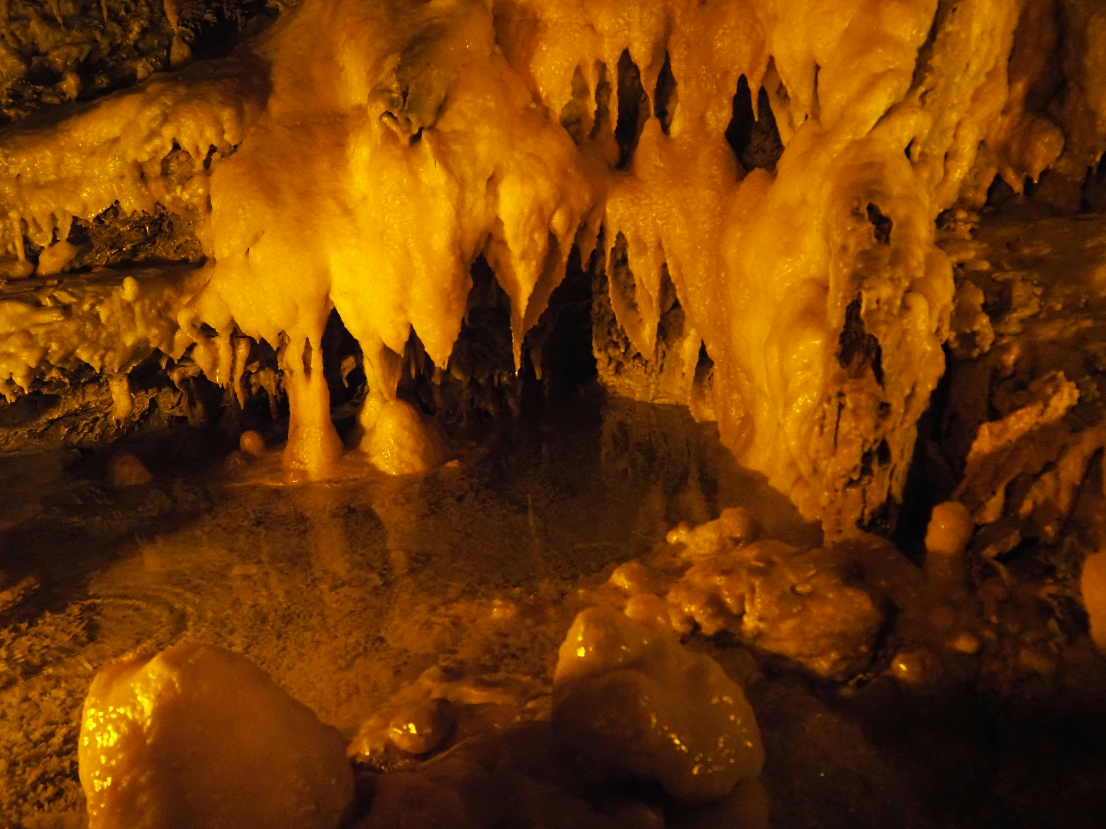 Höhle mit orangefarbenen Stalaktiten und Wasserpfütze