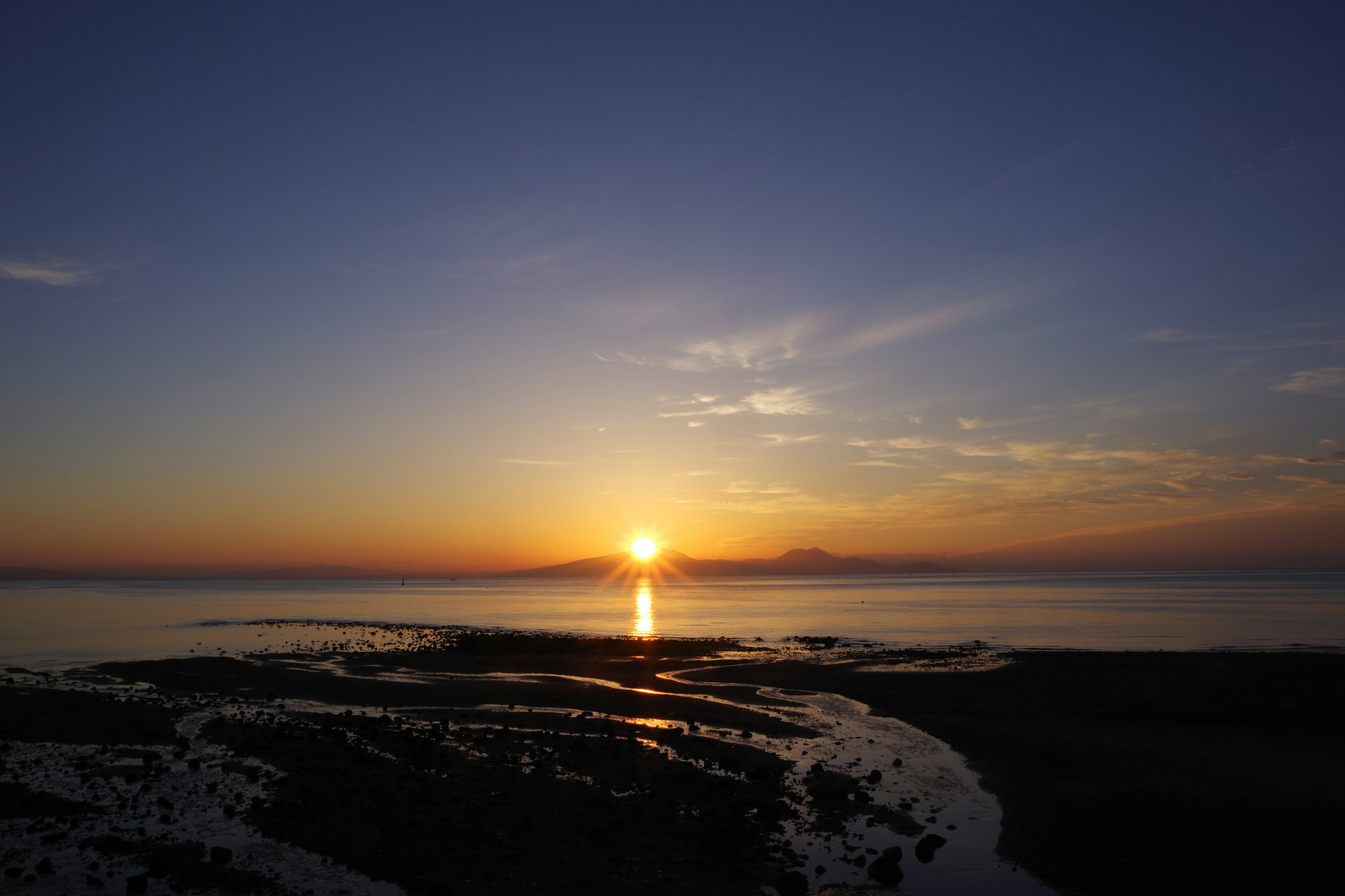 夕日が海に沈む風景 青とオレンジのグラデーション 浜辺の岩と水面の反射