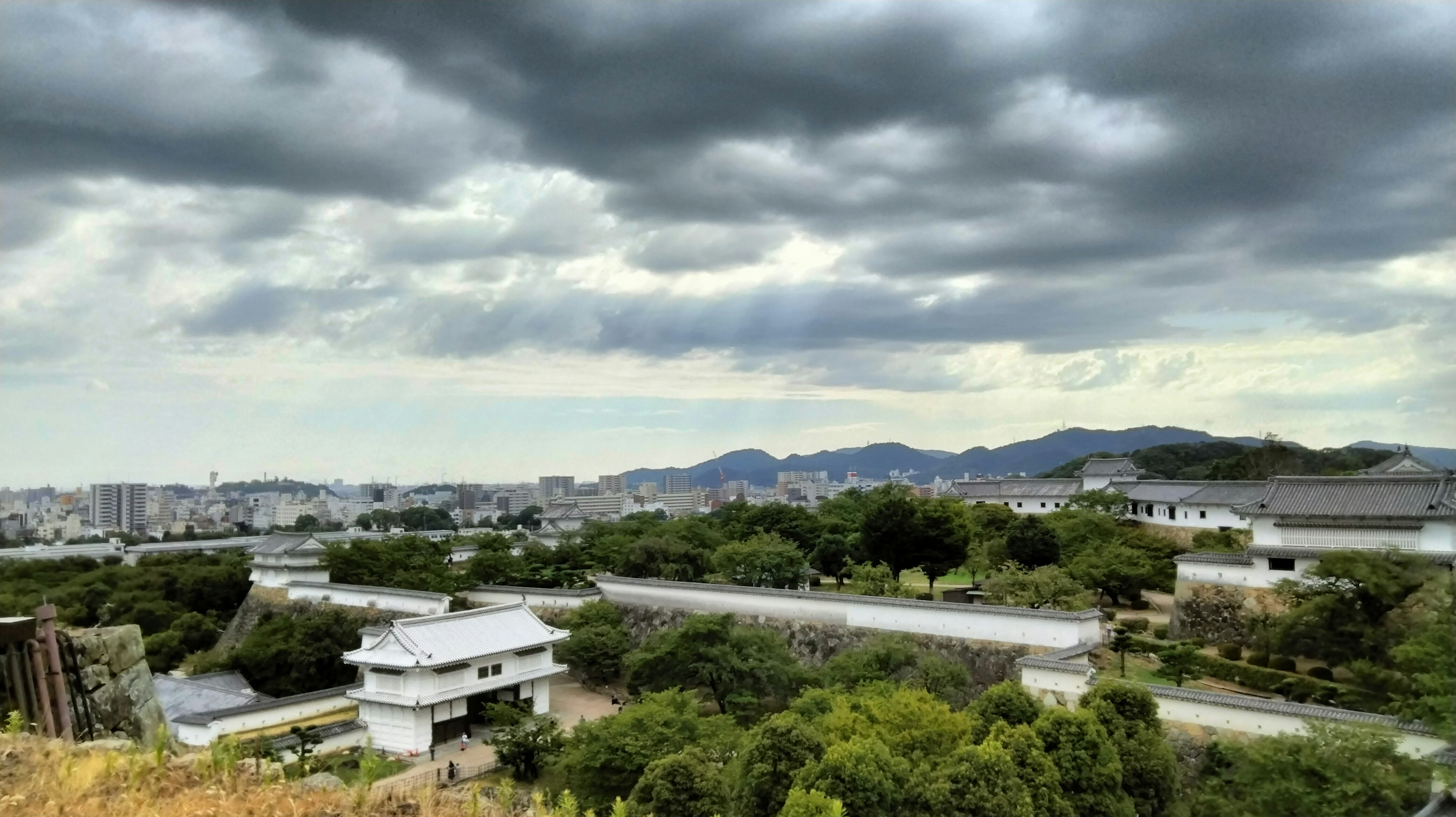 A landscape featuring dark clouds in the sky with lush green trees and a river