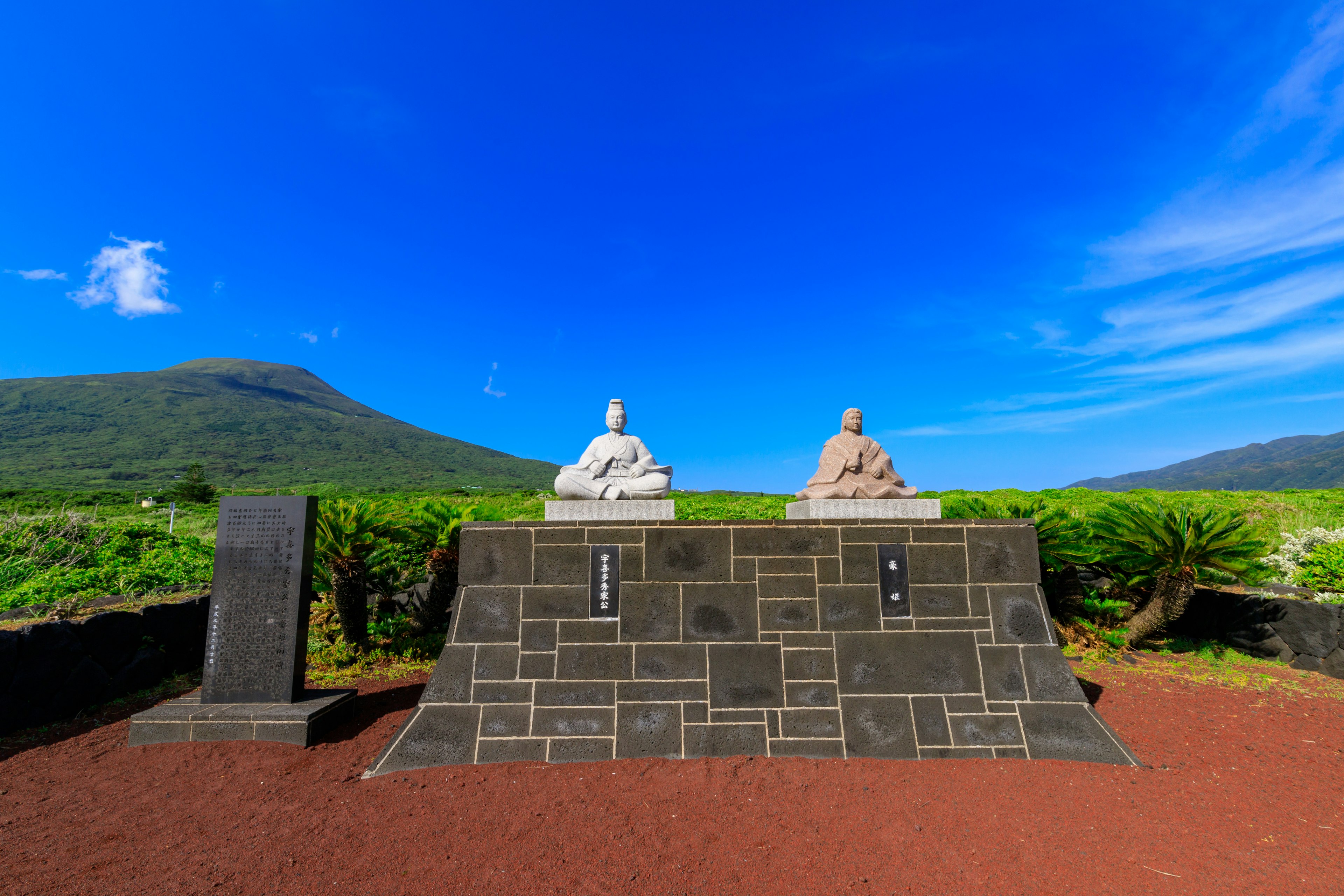 Two seated statues under a blue sky with a mountain backdrop