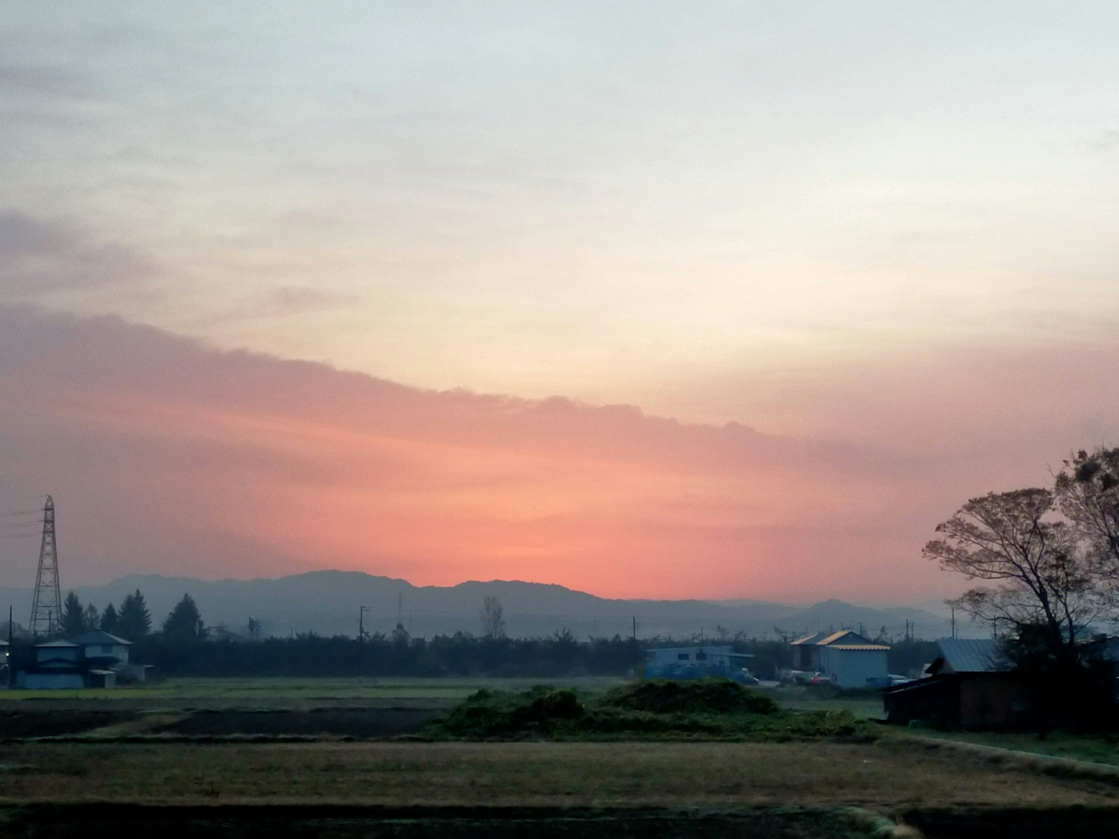 Pemandangan matahari terbenam dengan siluet ladang dan gunung jauh