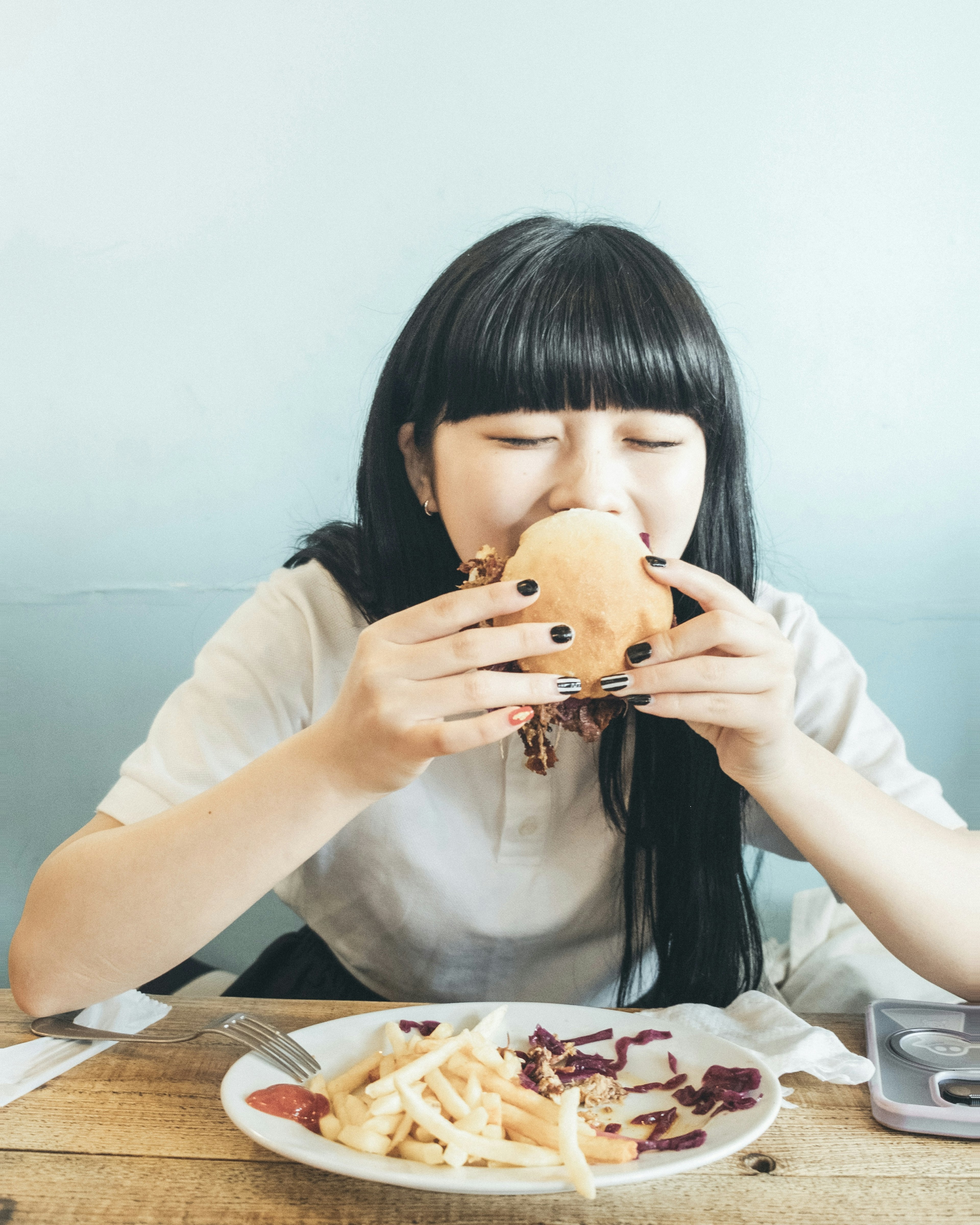 여성이 접시 위의 감자튀김과 함께 햄버거를 먹으려는 장면