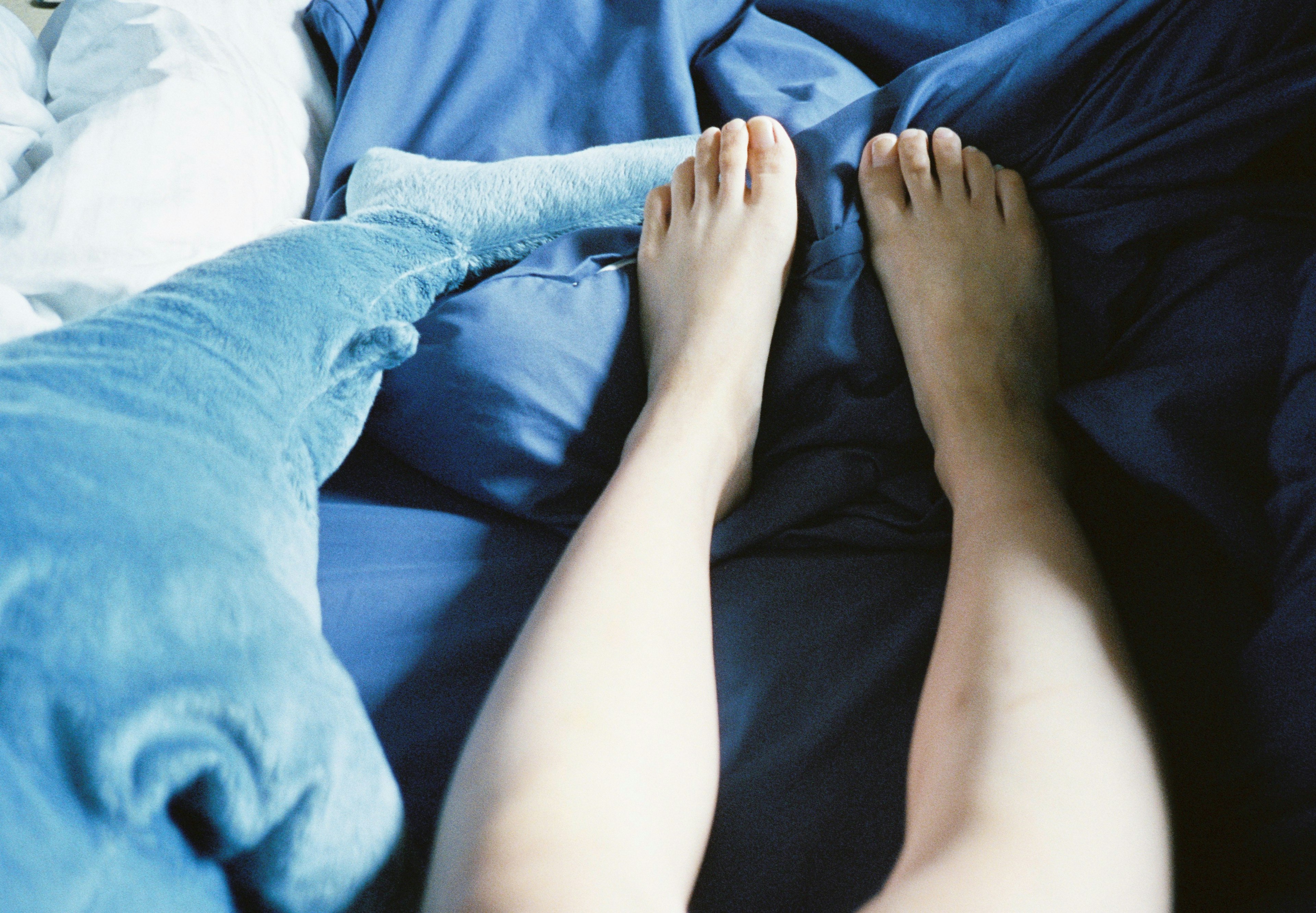 Two feet resting on blue sheets with a plush whale