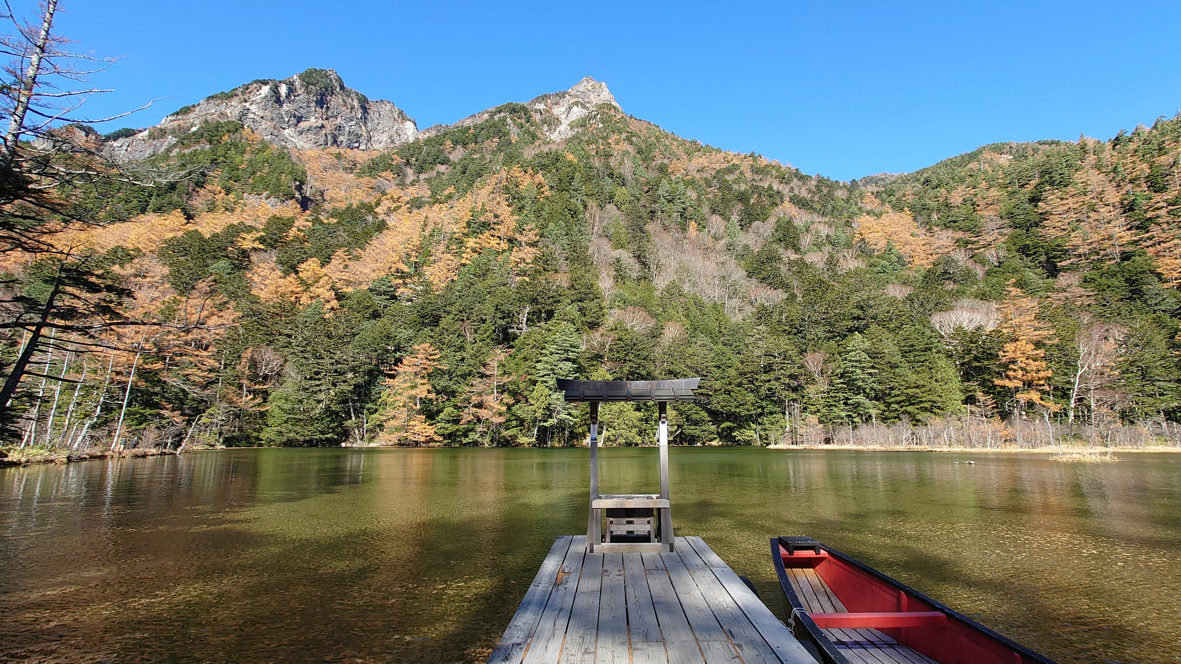 ทิวทัศน์ที่สวยงามของทะเลสาบที่เงียบสงบและภูเขาพร้อมท่าเรืออยู่ด้านหน้าแสดงสีสันของฤดูใบไม้ร่วง