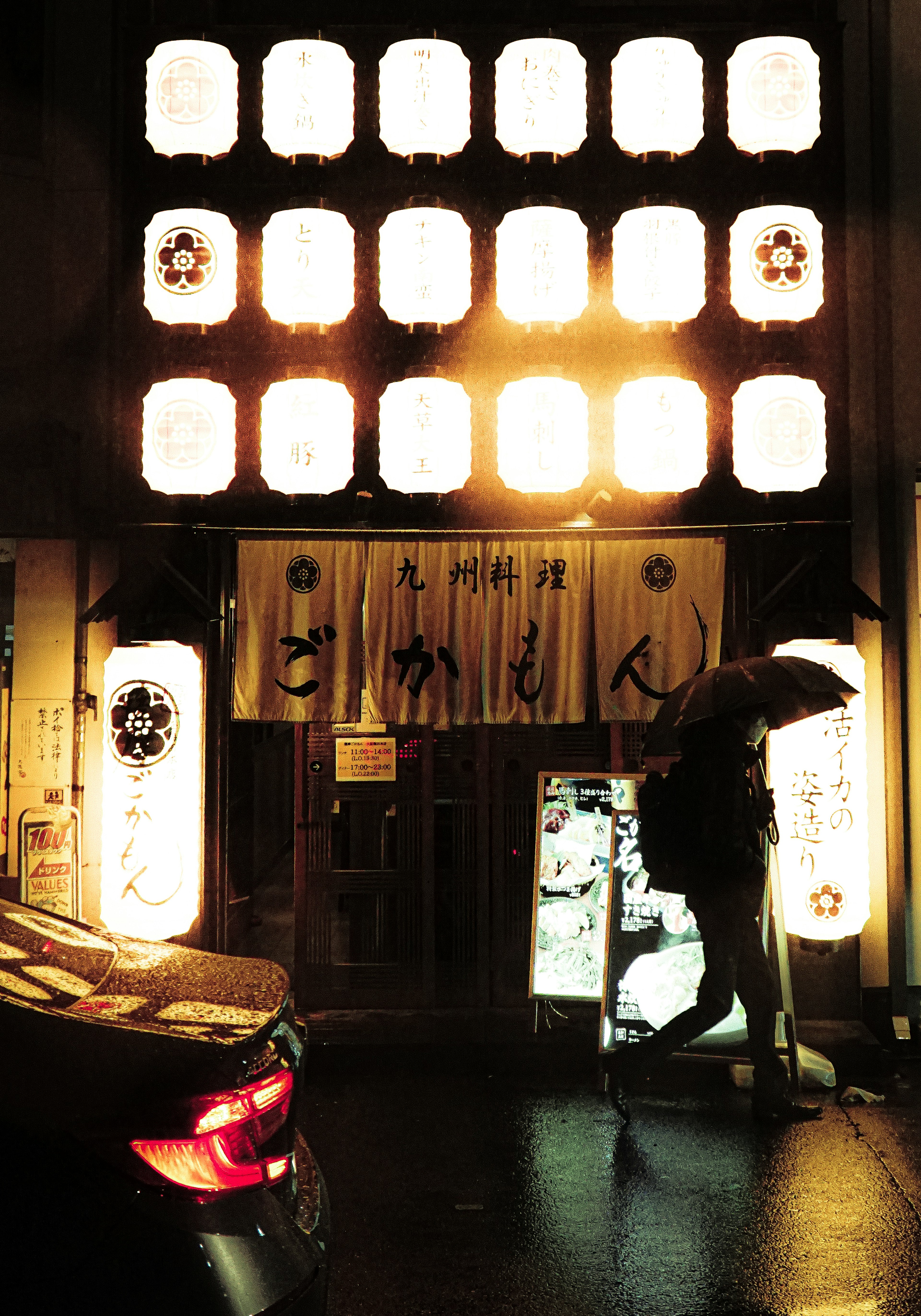 Extérieur d'un restaurant japonais traditionnel avec des lanternes lumineuses et une personne tenant un parapluie