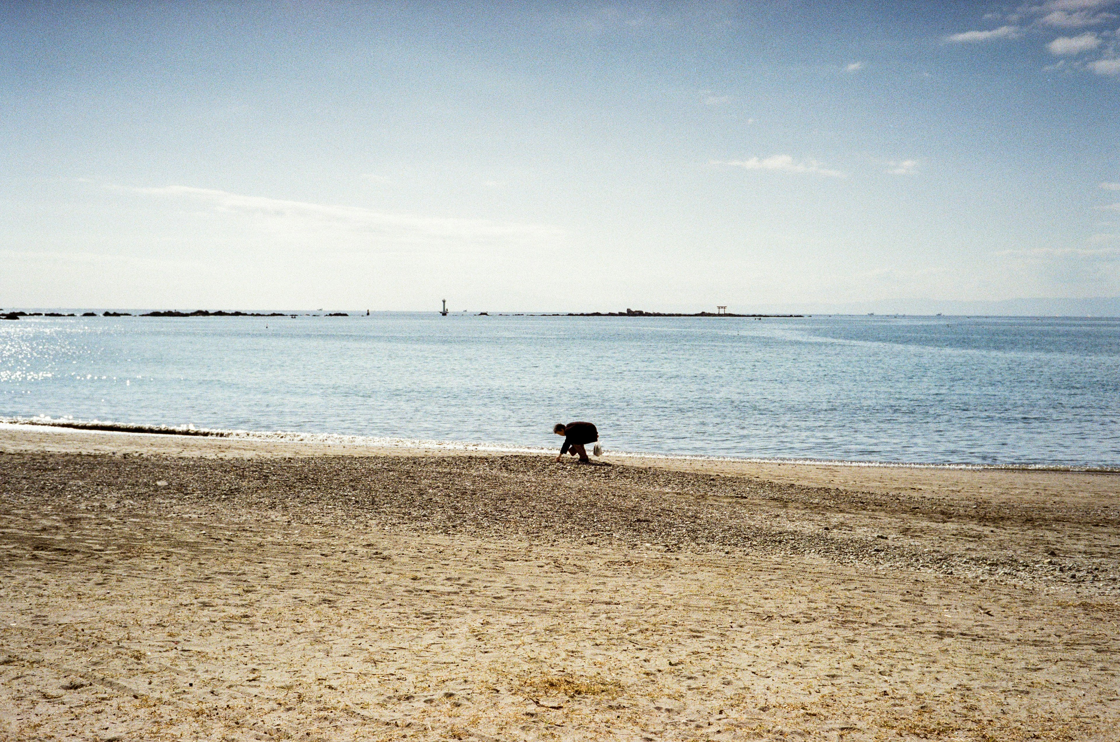 Person, die einen Hund an einem Sandstrand mit ruhiger See im Hintergrund spazieren führt