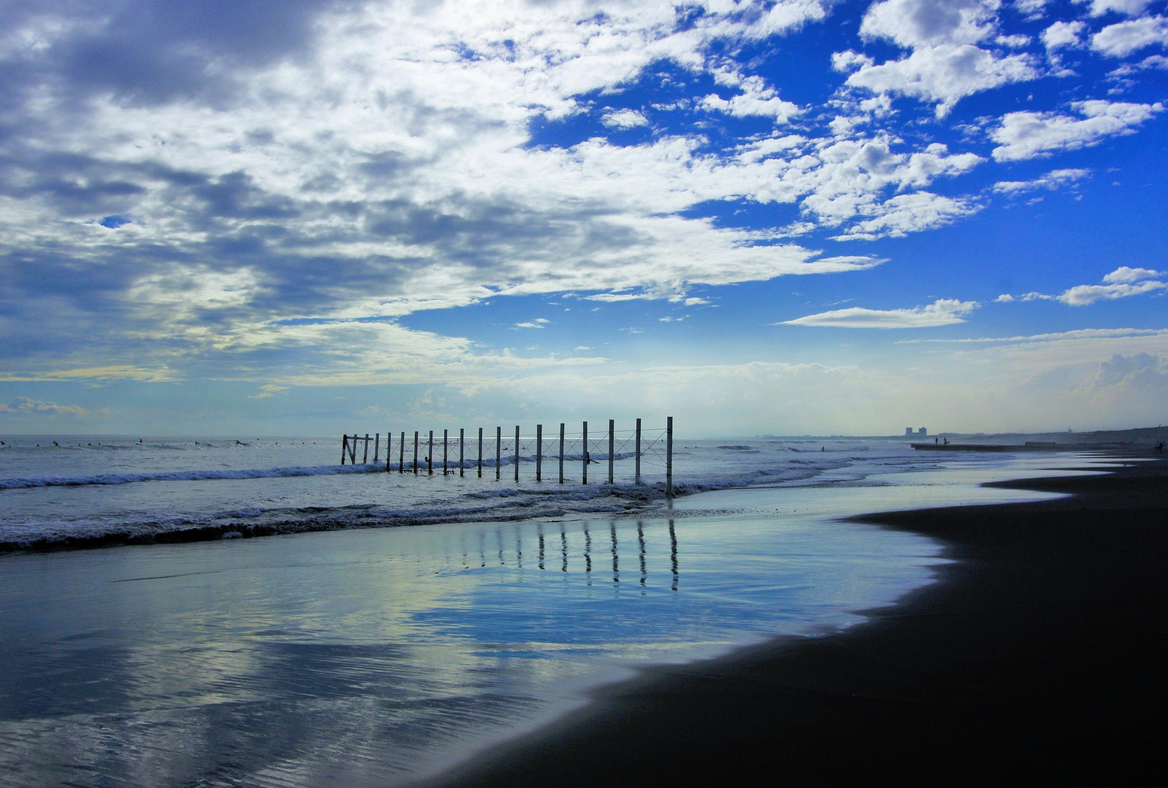 Coastal scene featuring black sand beach and reflections of blue sky and clouds