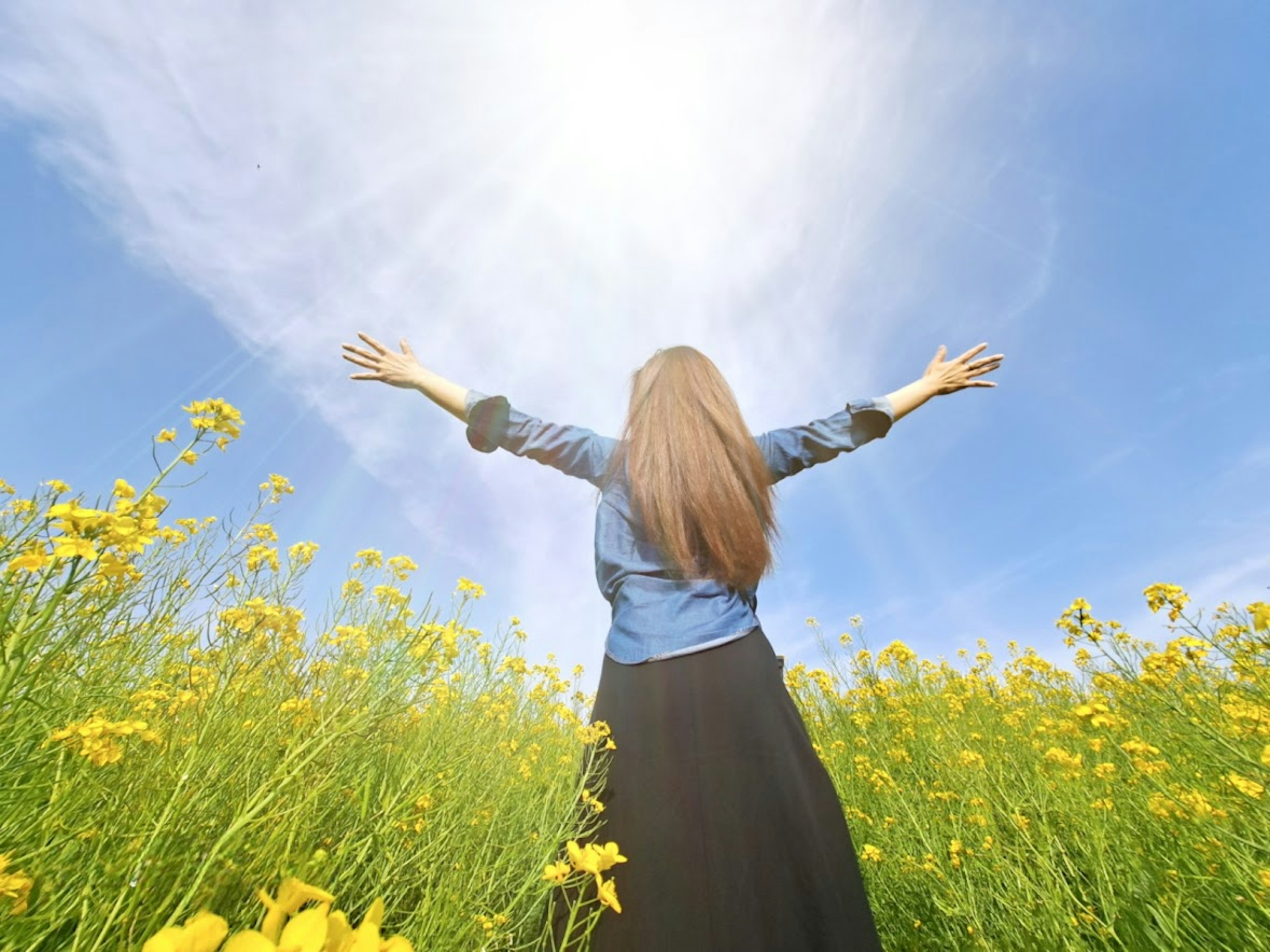 Femme les bras écartés dans un champ de fleurs jaunes sous un ciel bleu