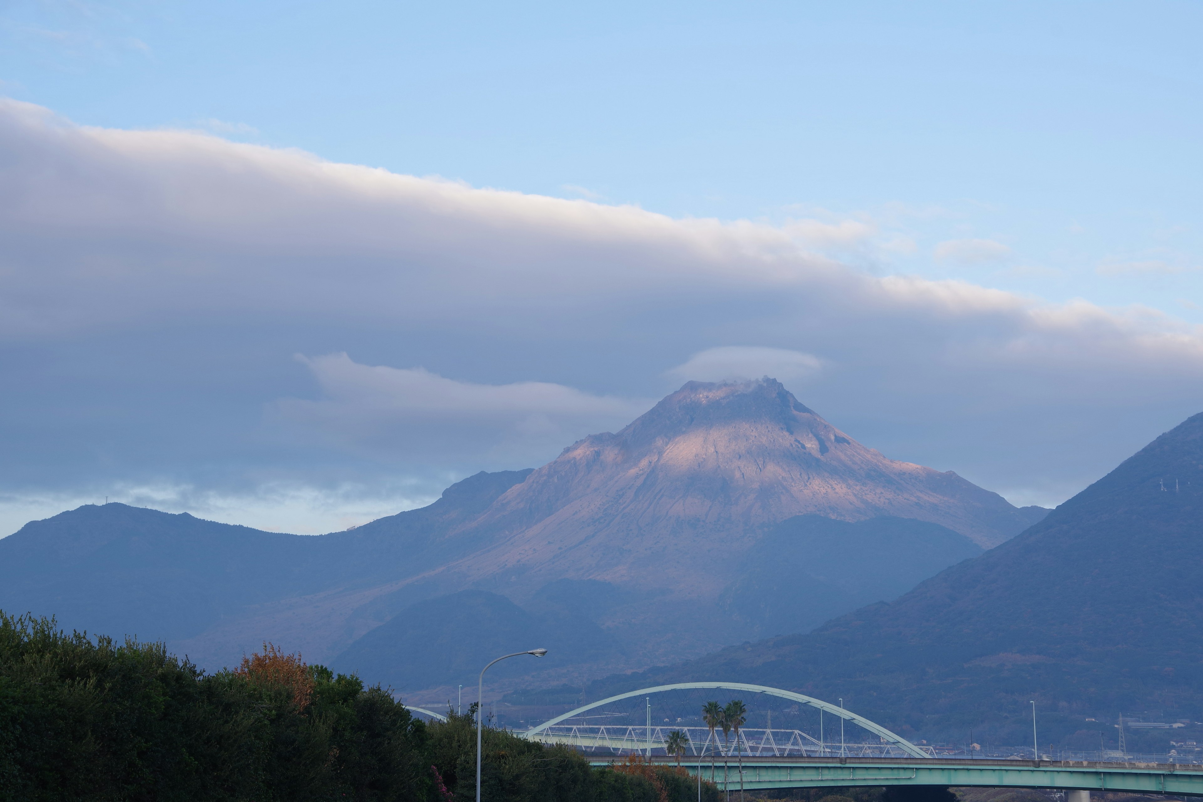 Mountain landscape with blue sky and clouds bridge visible in the foreground