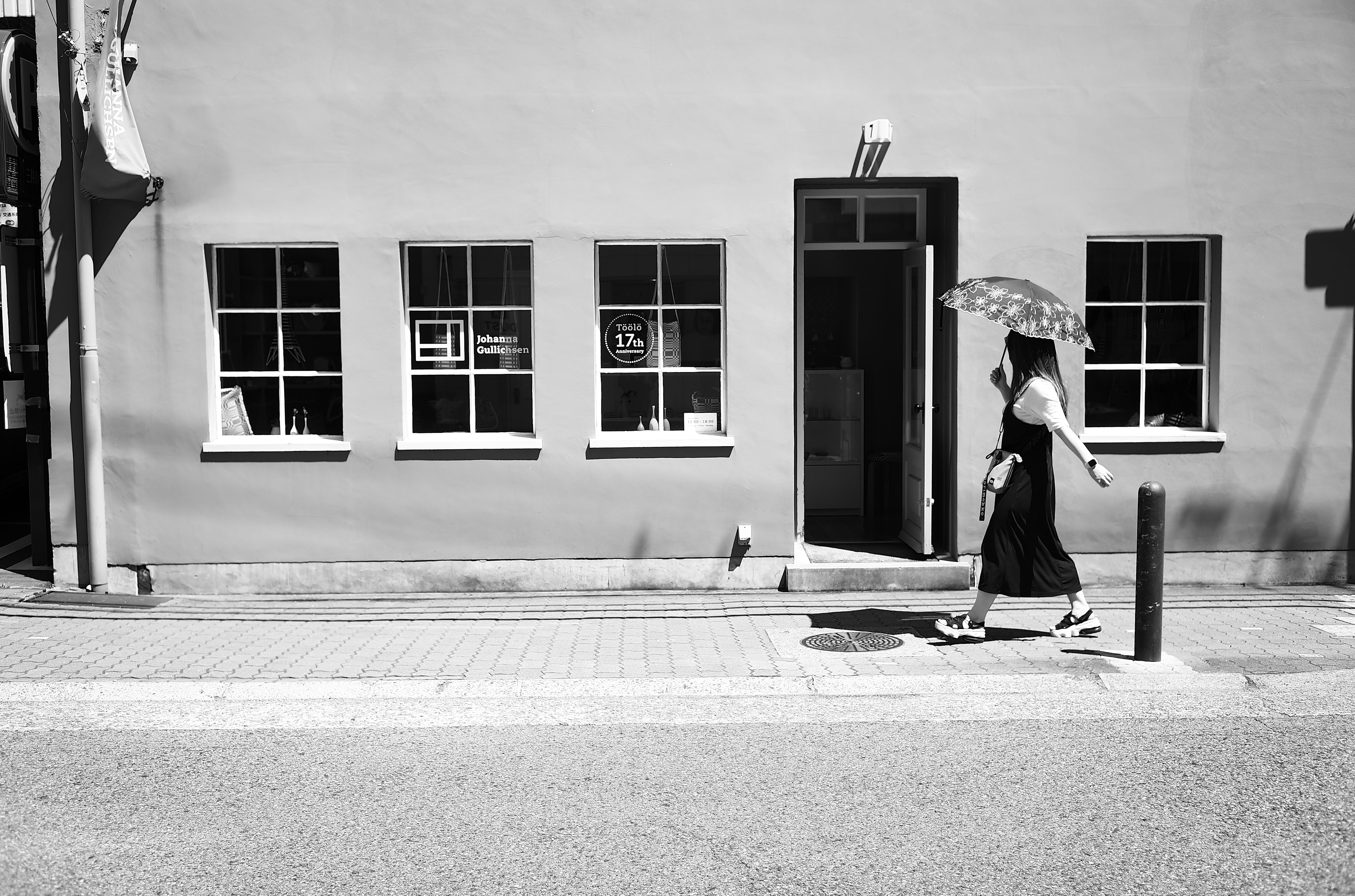 Una mujer con un vestido negro caminando con un parasol en una escena de calle en blanco y negro