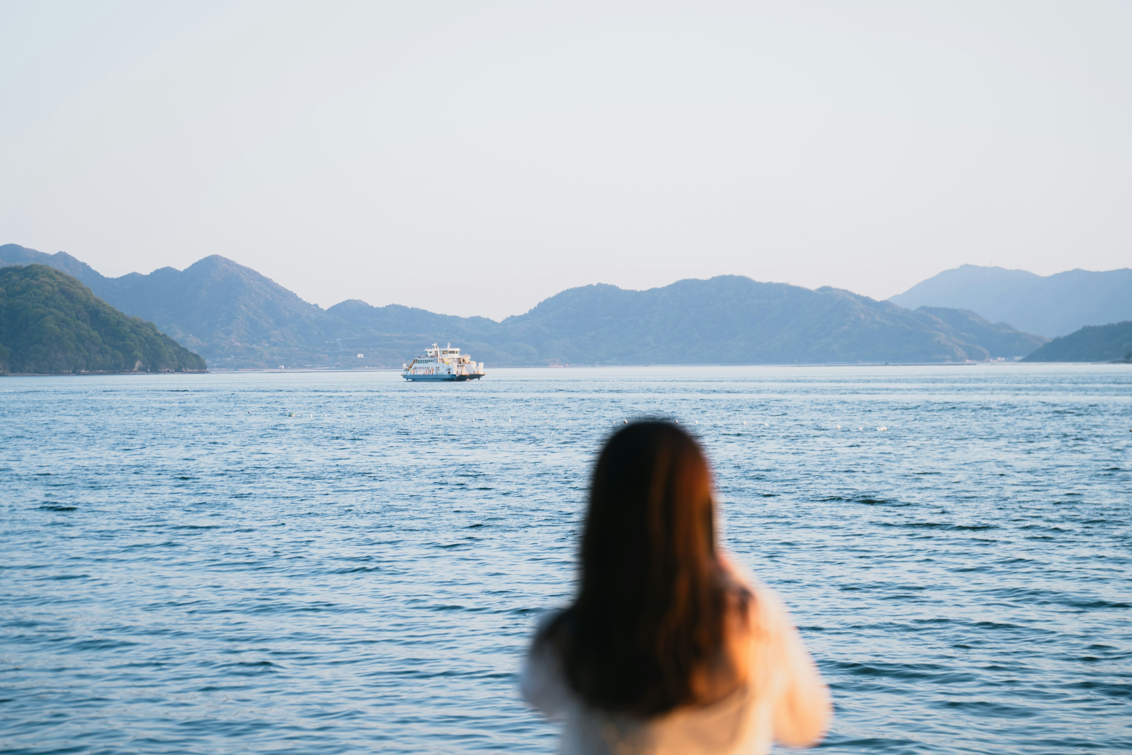 Frau, die aufs Meer schaut mit entfernten Bergen