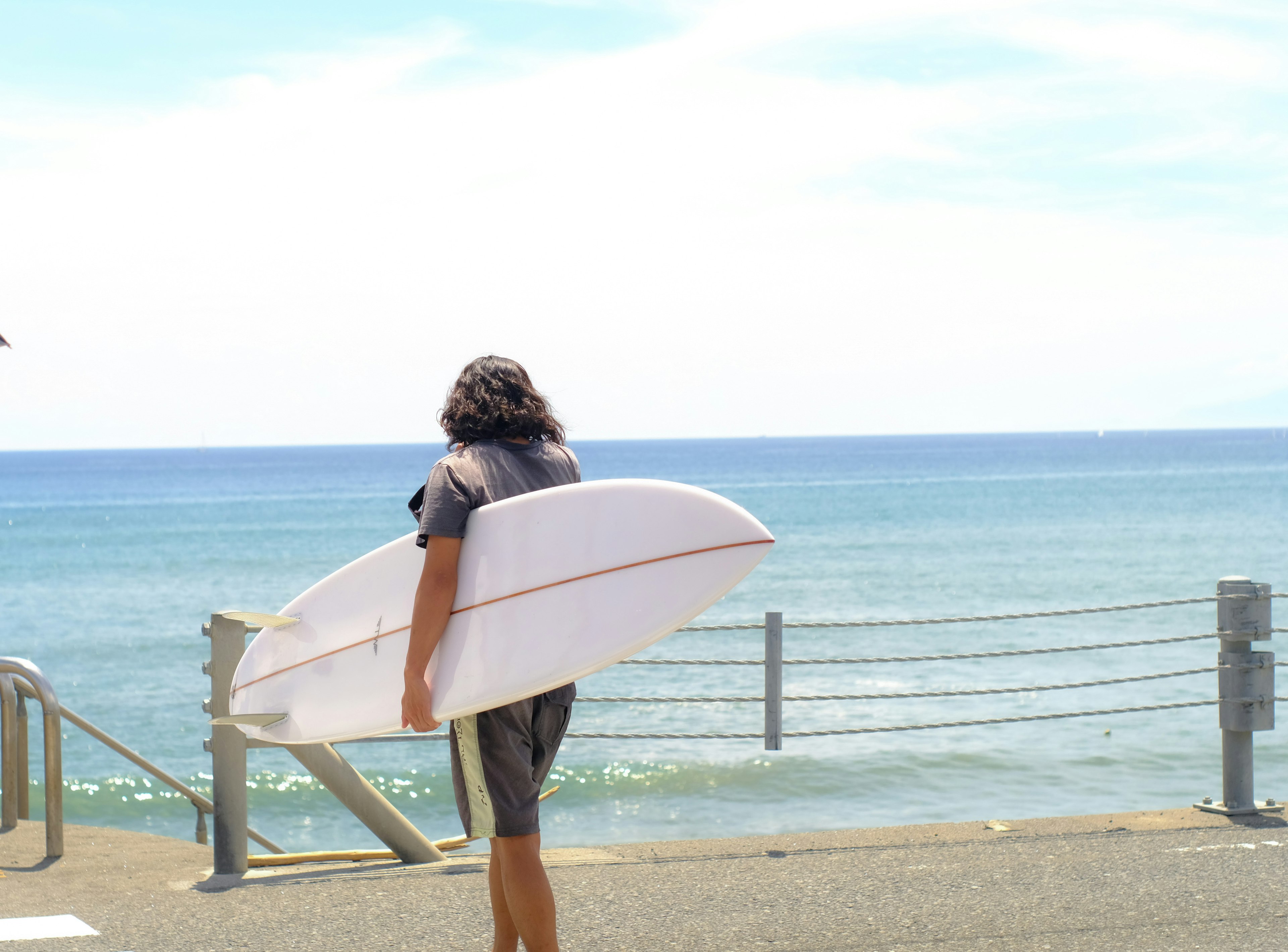 サーフボードを持ったサーフィンをする人が海を見つめている