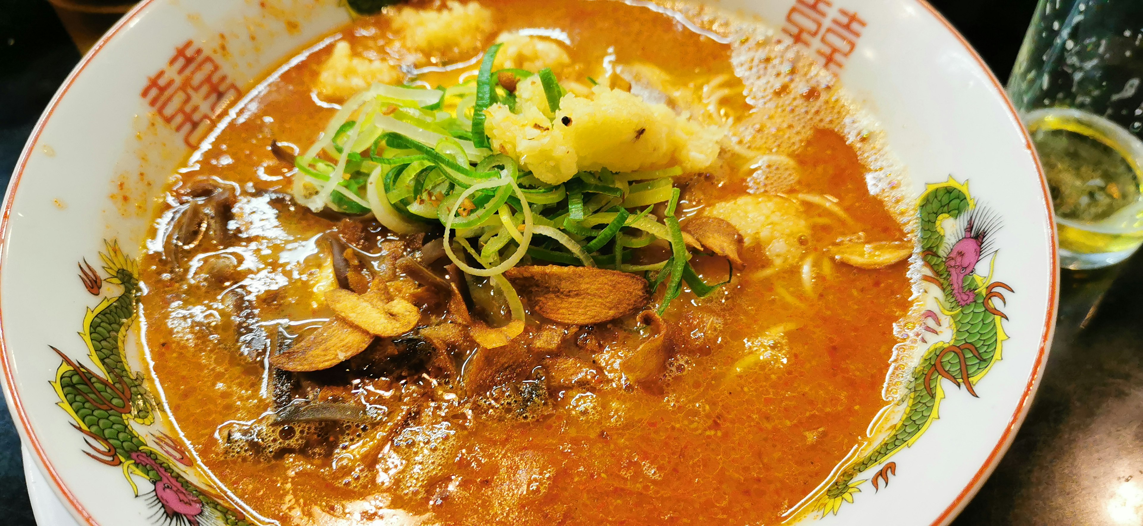 Bol de ramen avec une soupe rougeâtre garni d'oignons verts et de palourdes