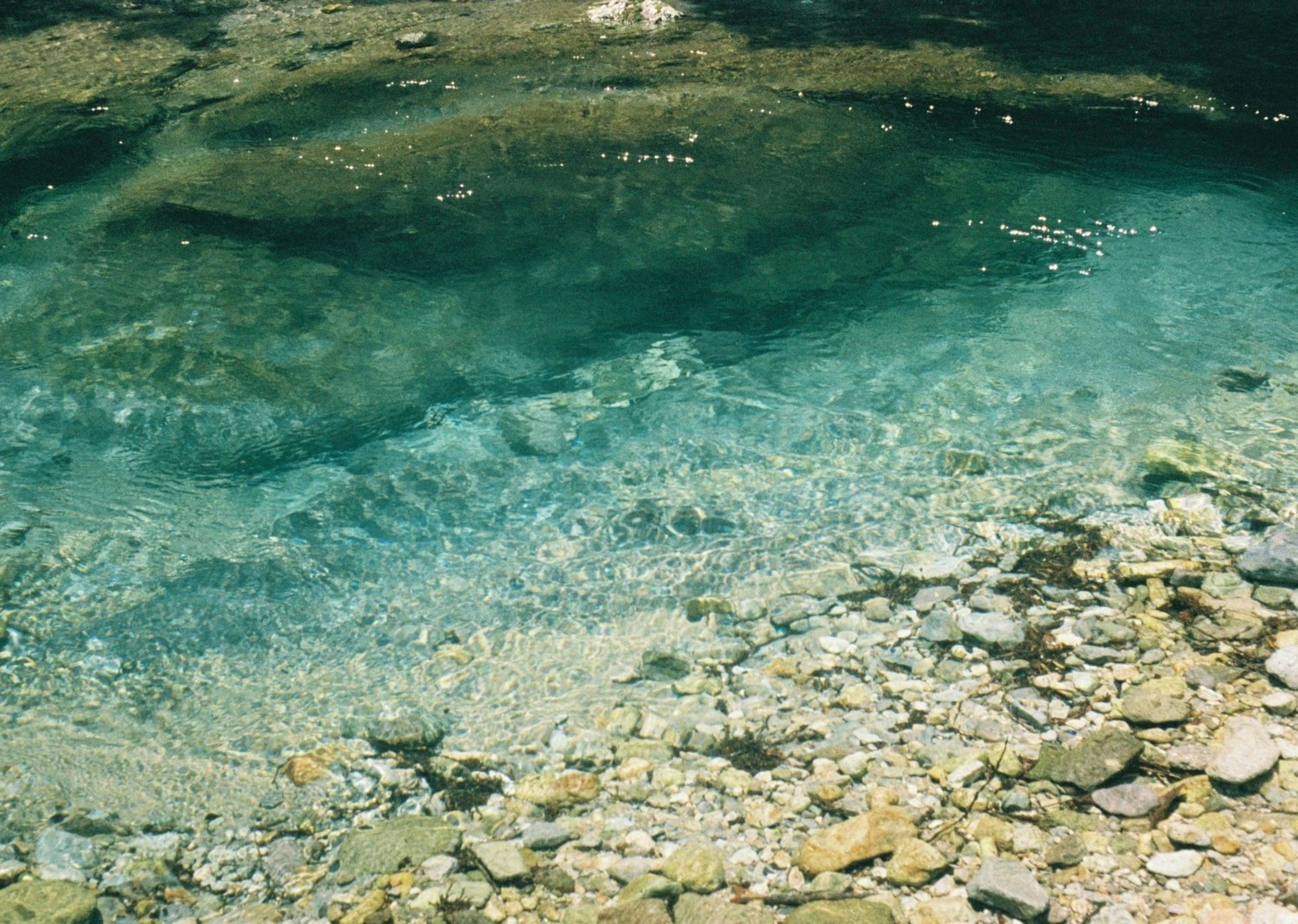 Air jernih di atas batu halus di dasar sungai yang tenang