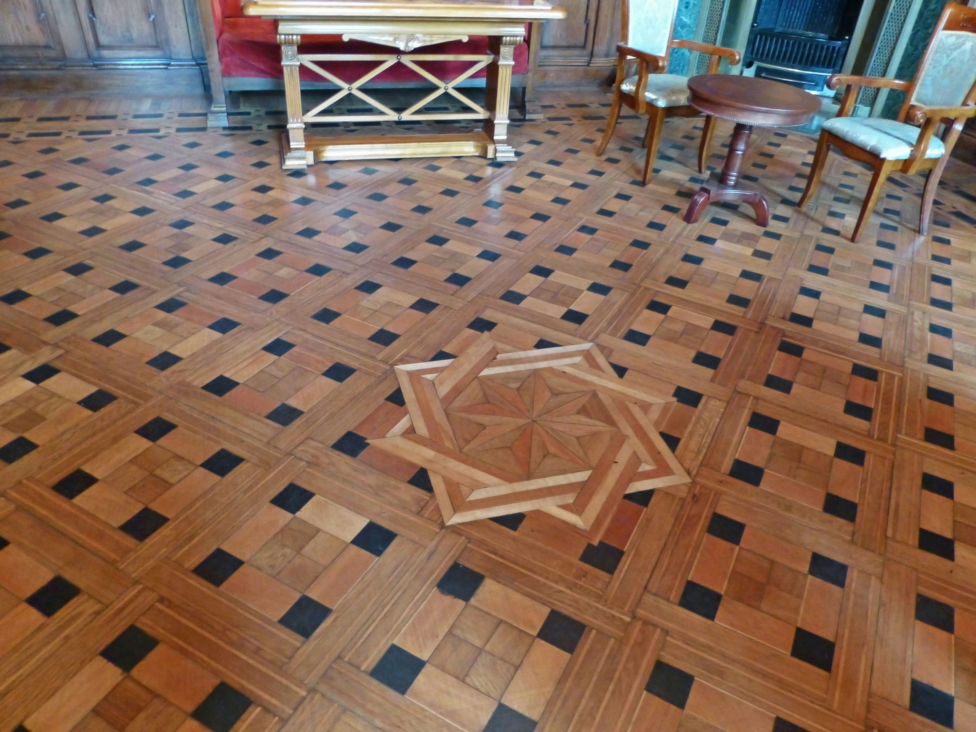 Intérieur d'une pièce avec un sol en bois présentant des carreaux noirs et marron une table et des chaises sont visibles