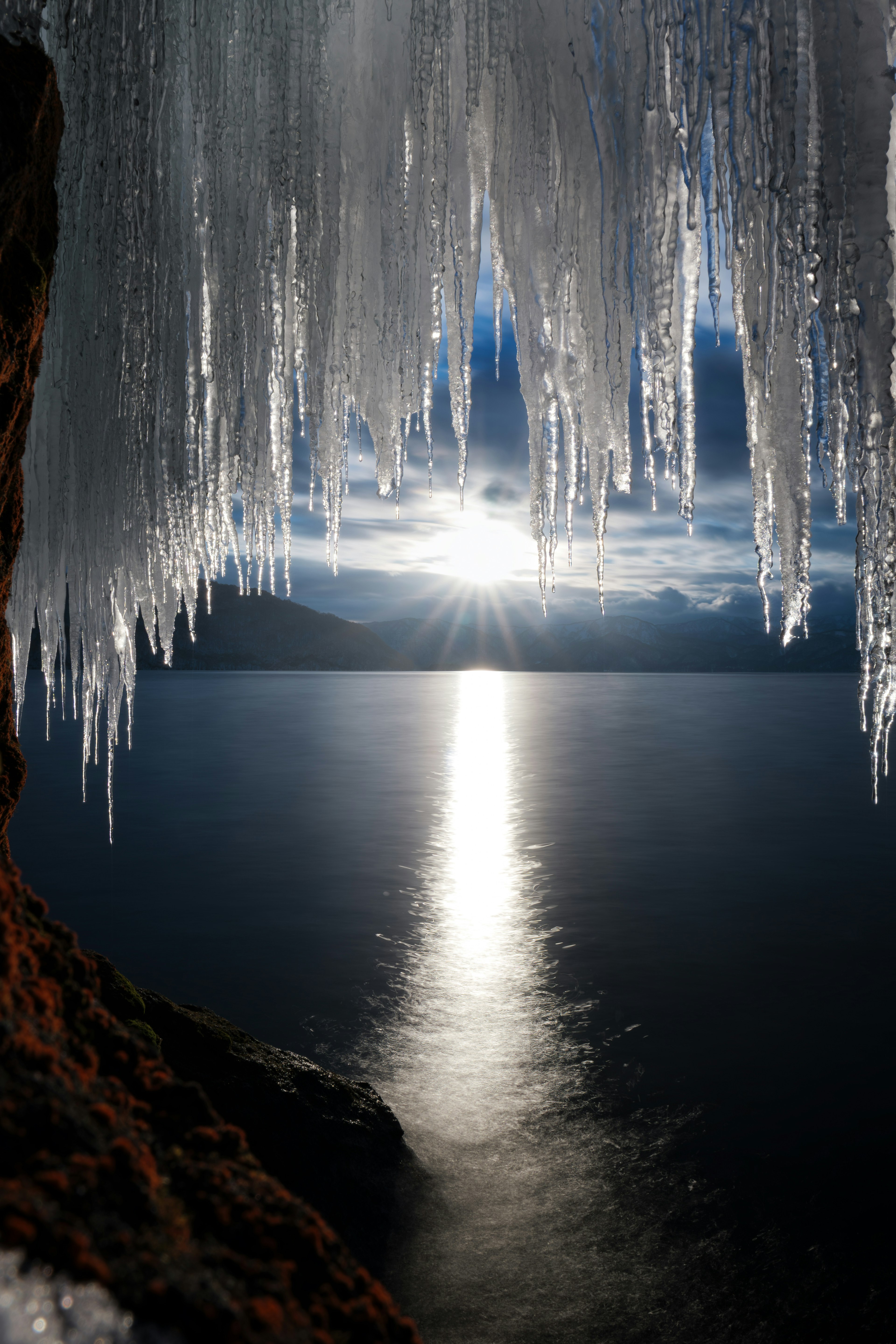 Icicles hanging from rocks overlooking a lake Sun reflecting on the water's surface