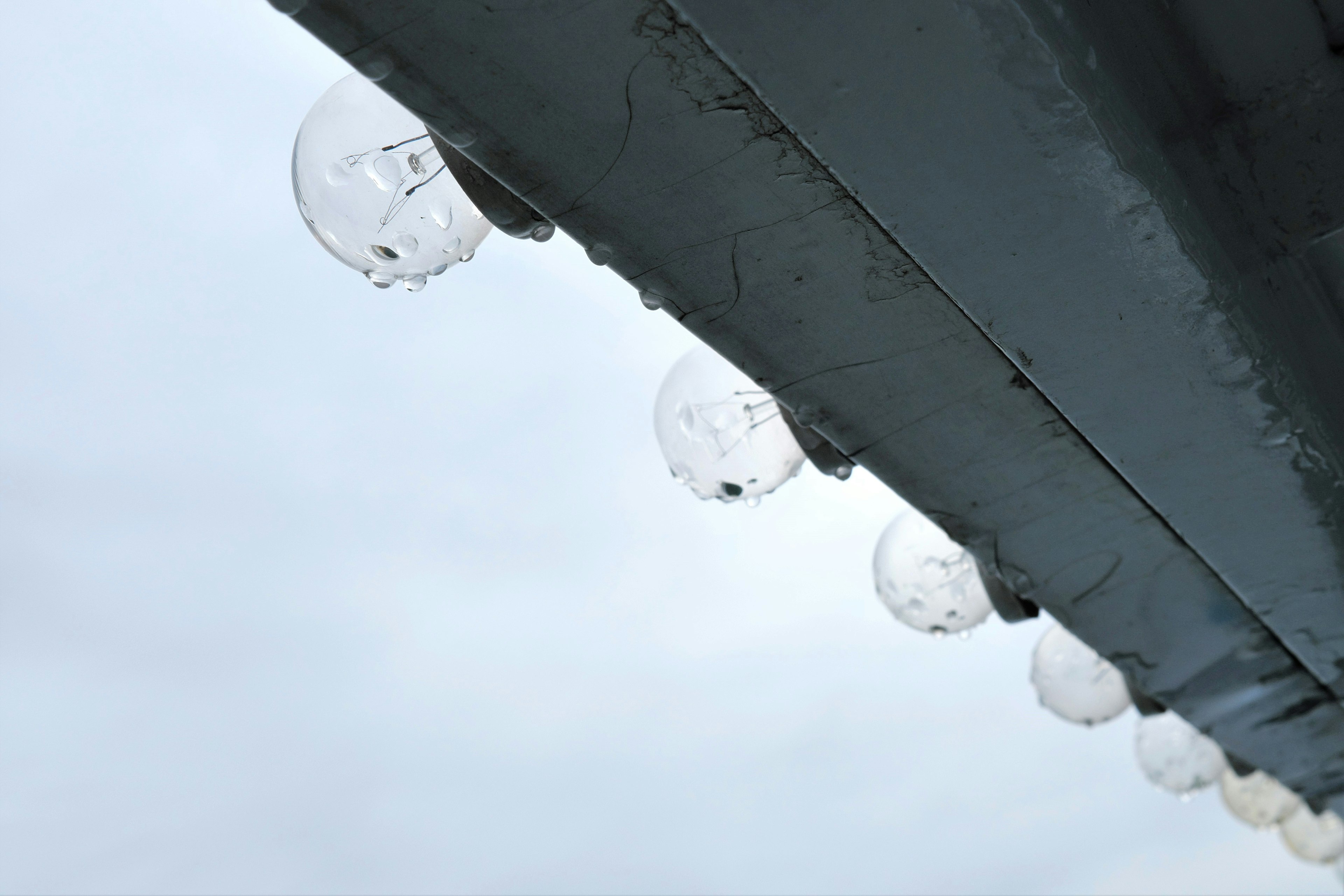 Transparent spherical lamps hanging under a roof in the rain