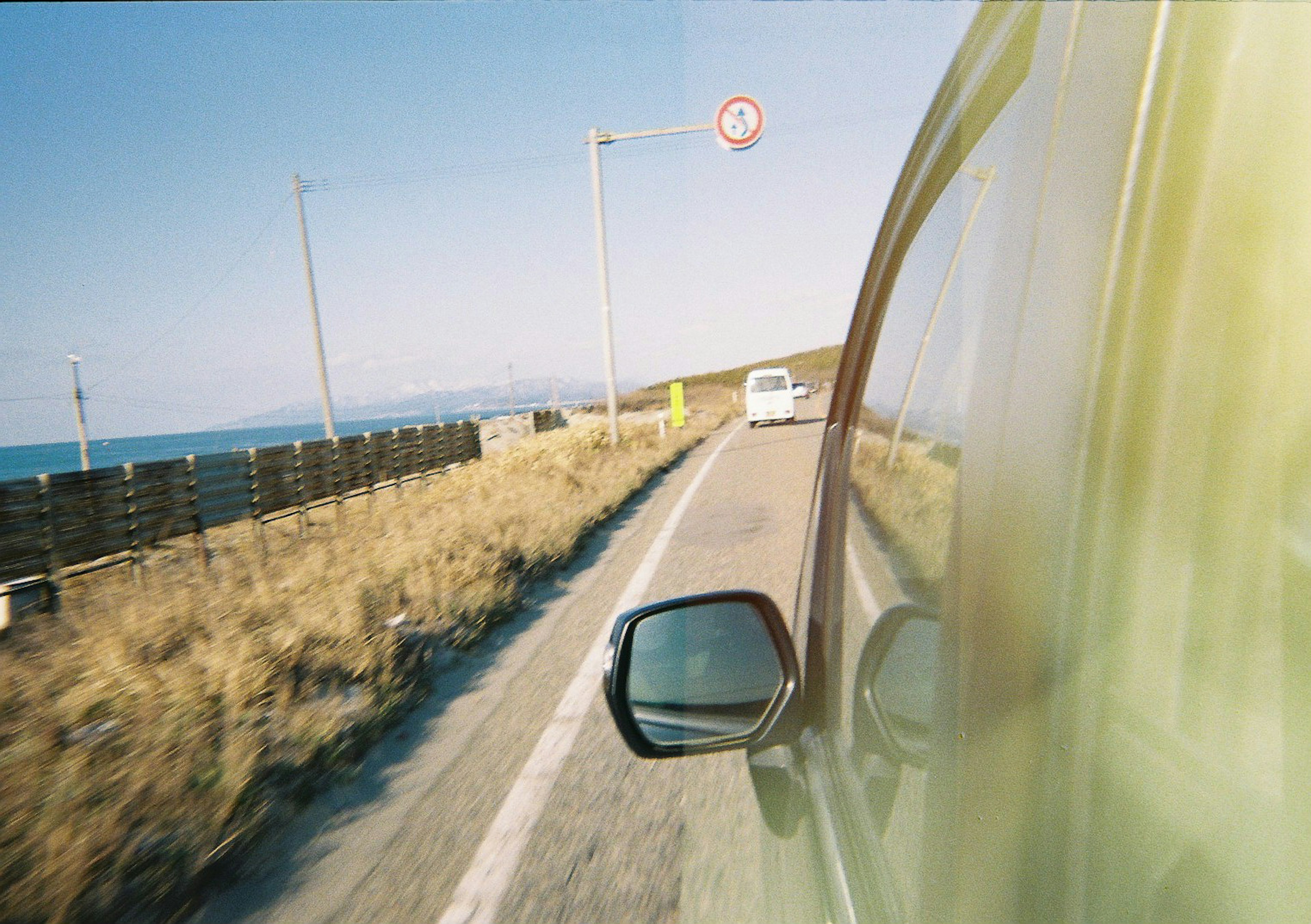 Blick auf ein Auto, das entlang einer Küstenstraße fährt, mit dem Meer im Hintergrund