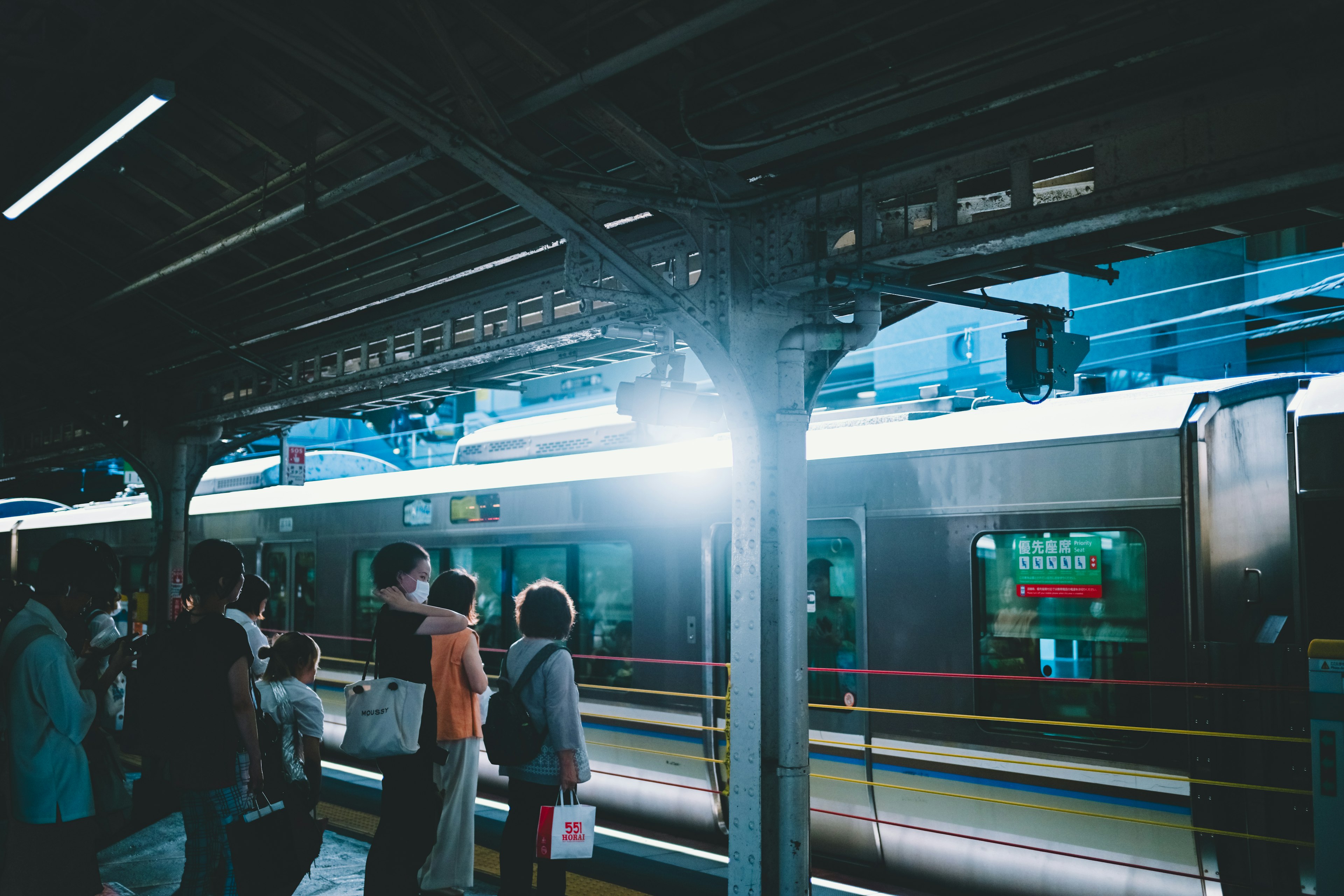 Menschen warten an einem Bahnhof mit einem von blauem Licht beleuchteten Zug