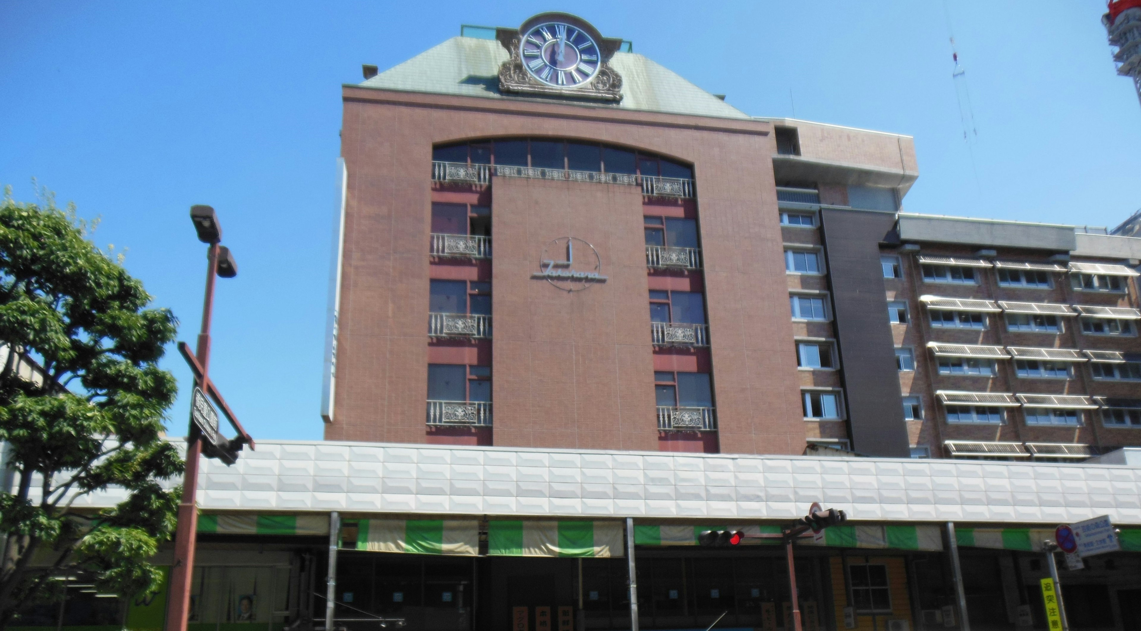 Exterior de un edificio con un reloj prominente árboles verdes y cielo azul de fondo