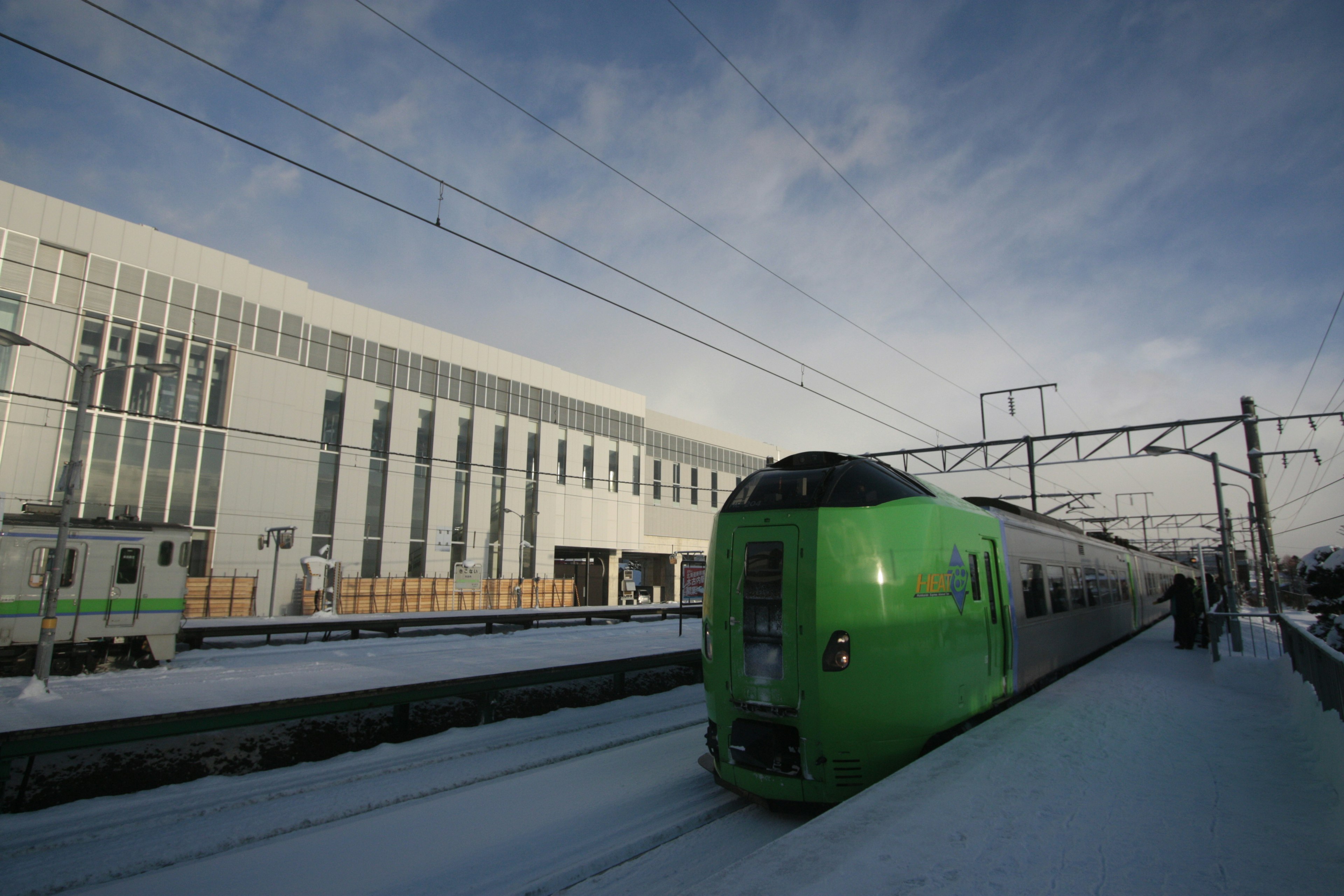 Green train at a snowy station with modern architecture