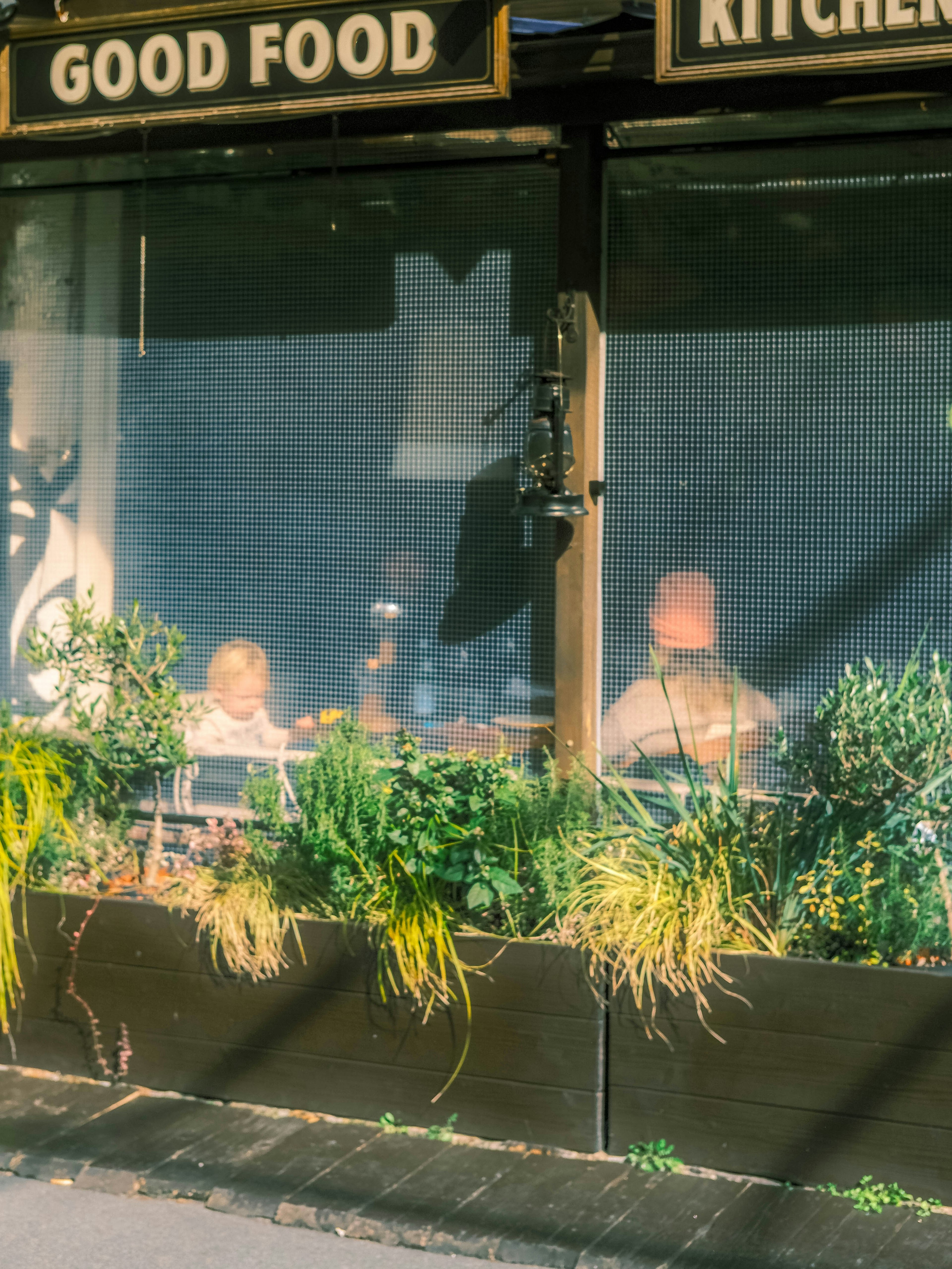 Café-Außenansicht mit Kindern, die durch das Fenster sichtbar sind, und Pflanzen in Kästen