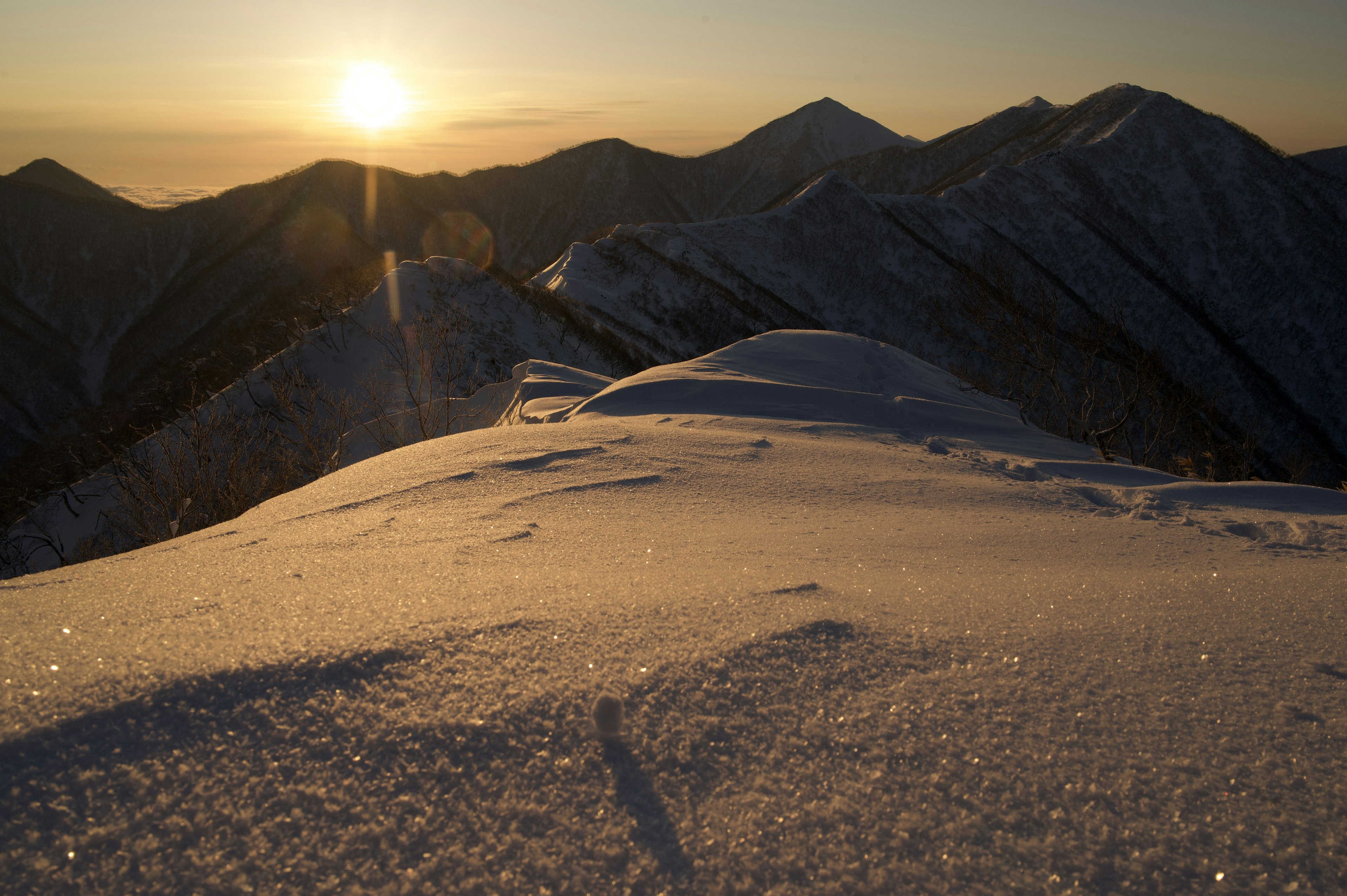 雪に覆われた山頂からの夕日と山々の風景