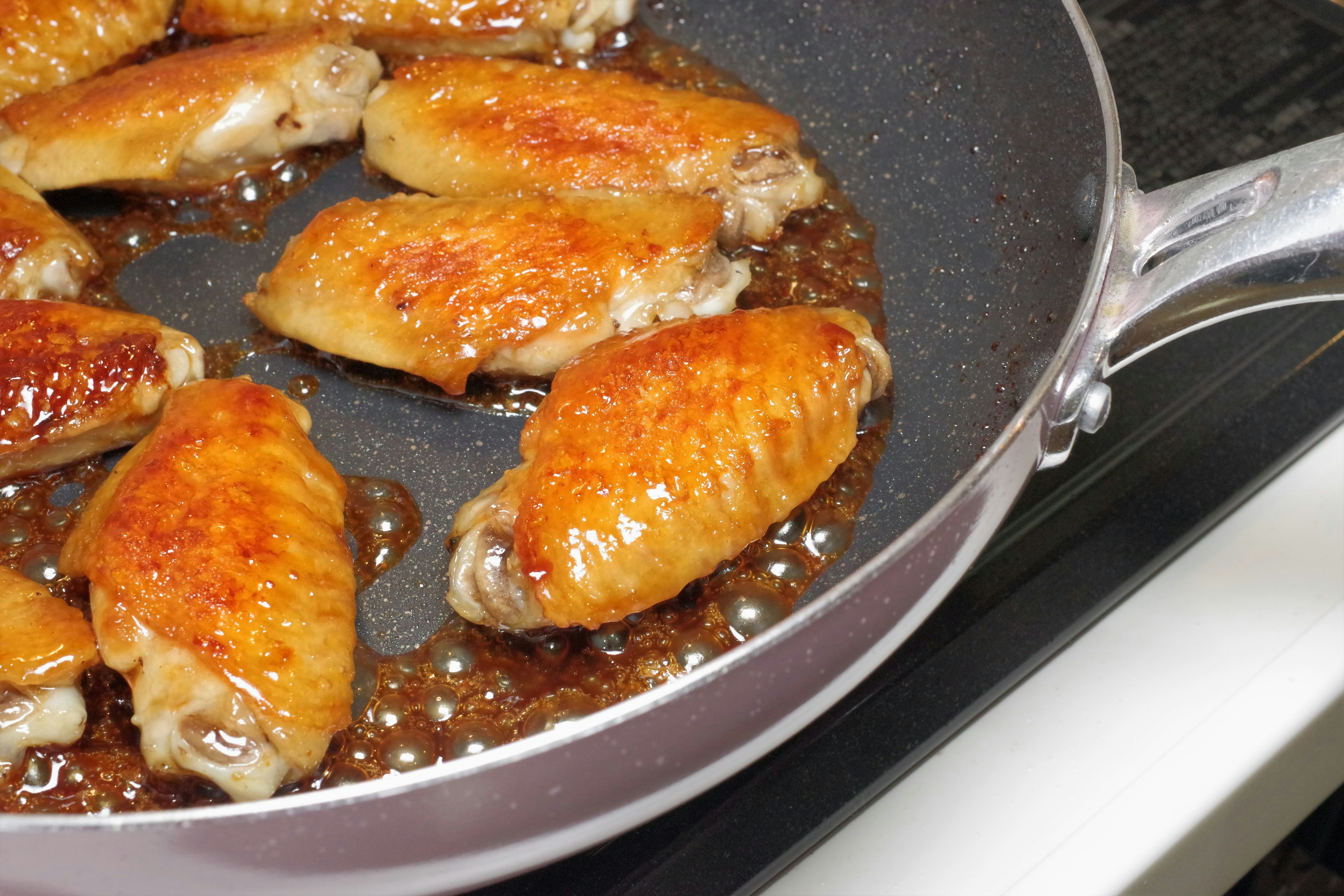 Cooked chicken wings sizzling in a frying pan